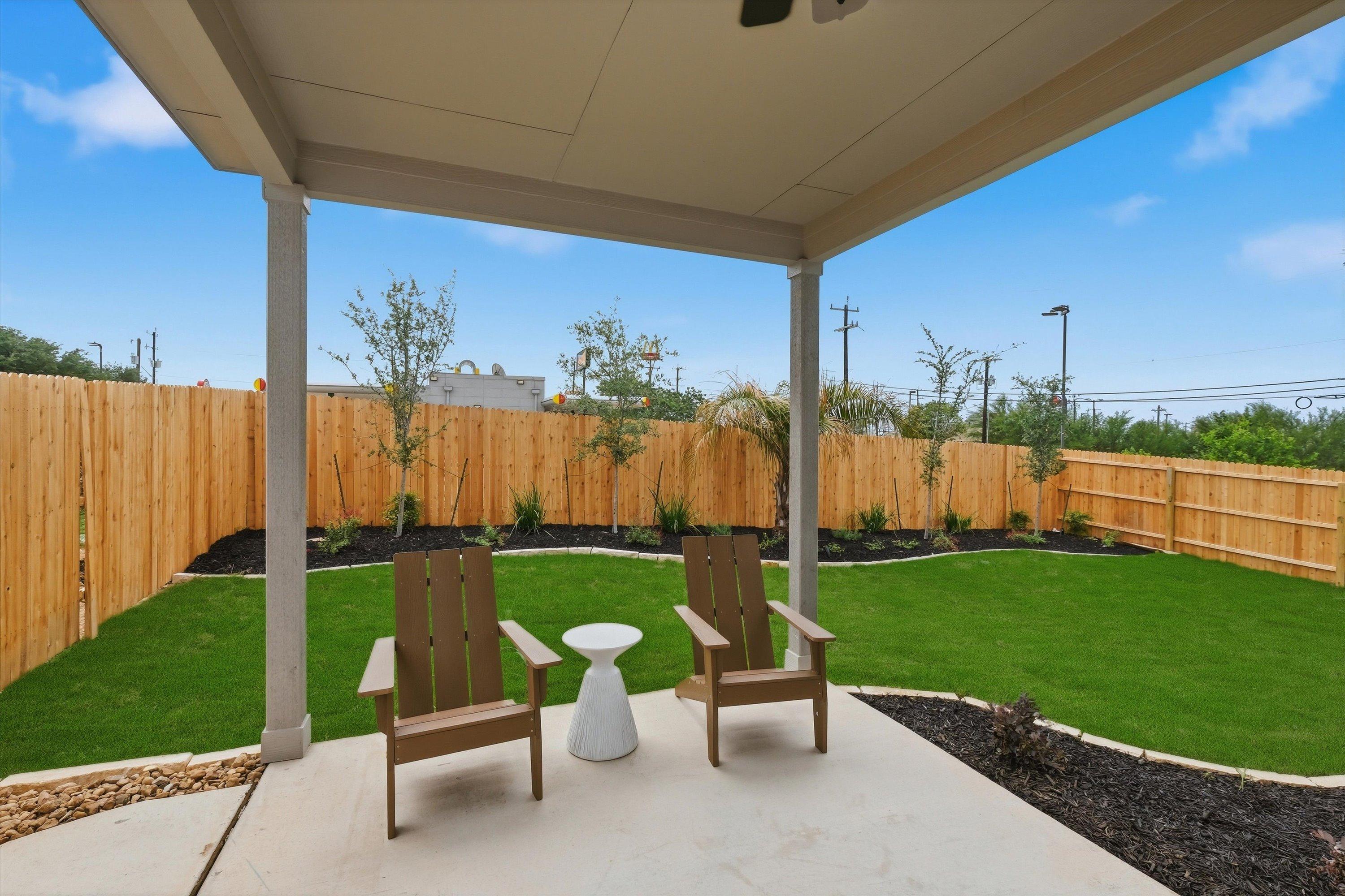 Covered patio with Adirondack chairs and side table at Rayburn Valley in San Antonio TX, featuring green lawn and privacy fence
