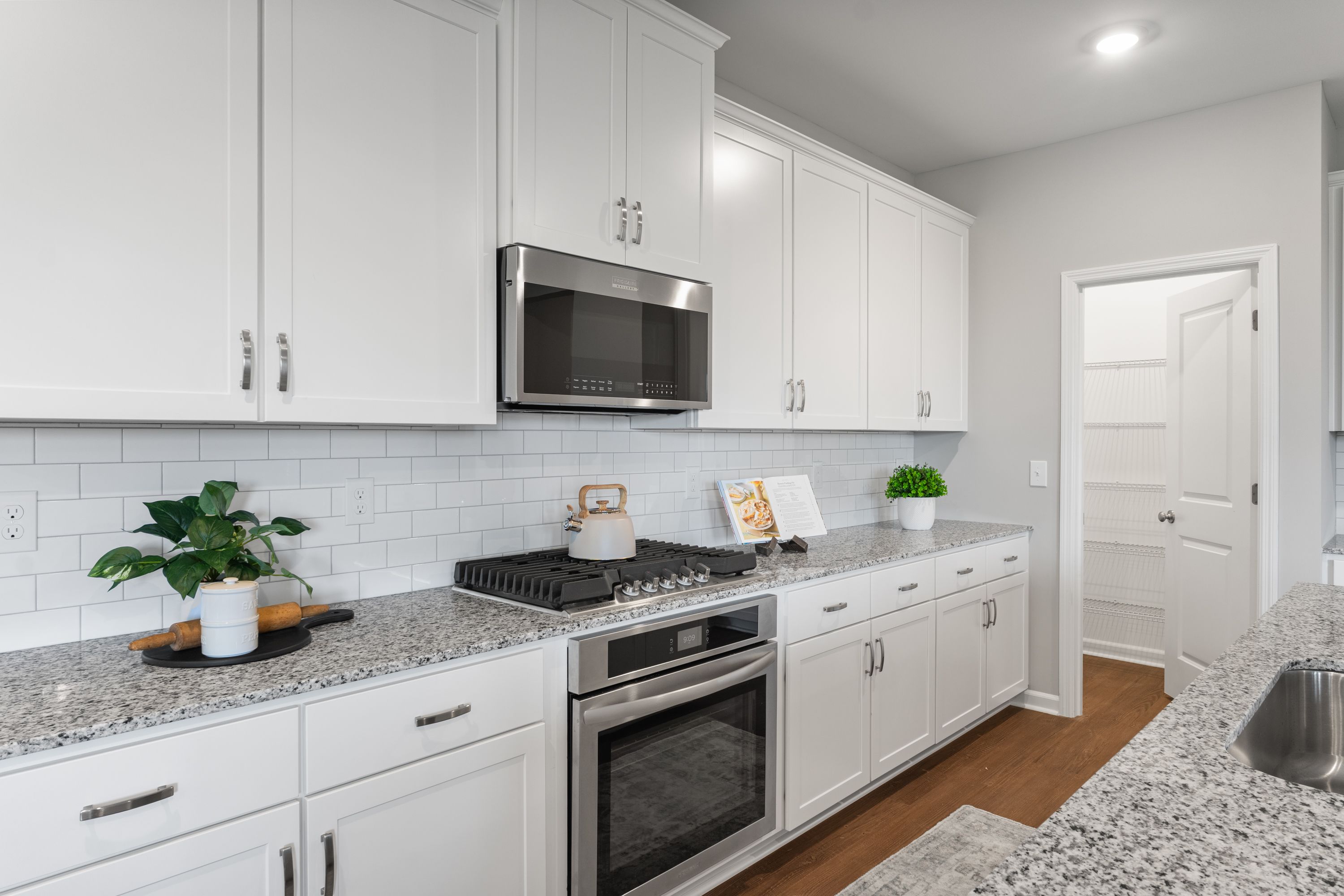 Spacious Avalon E kitchen featuring white shaker cabinets, granite counters, subway tile backsplash, and stainless steel appliances