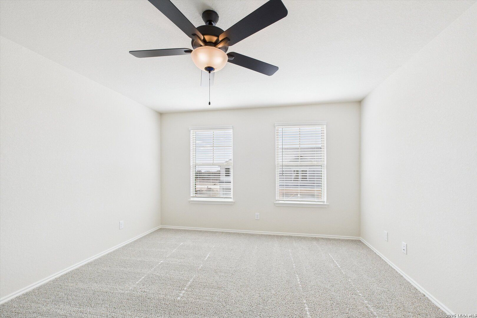 Bright secondary bedroom with ceiling fan, large windows, and carpeted floors in The Gillian B, Davidson Homes, San Antonio, Texas