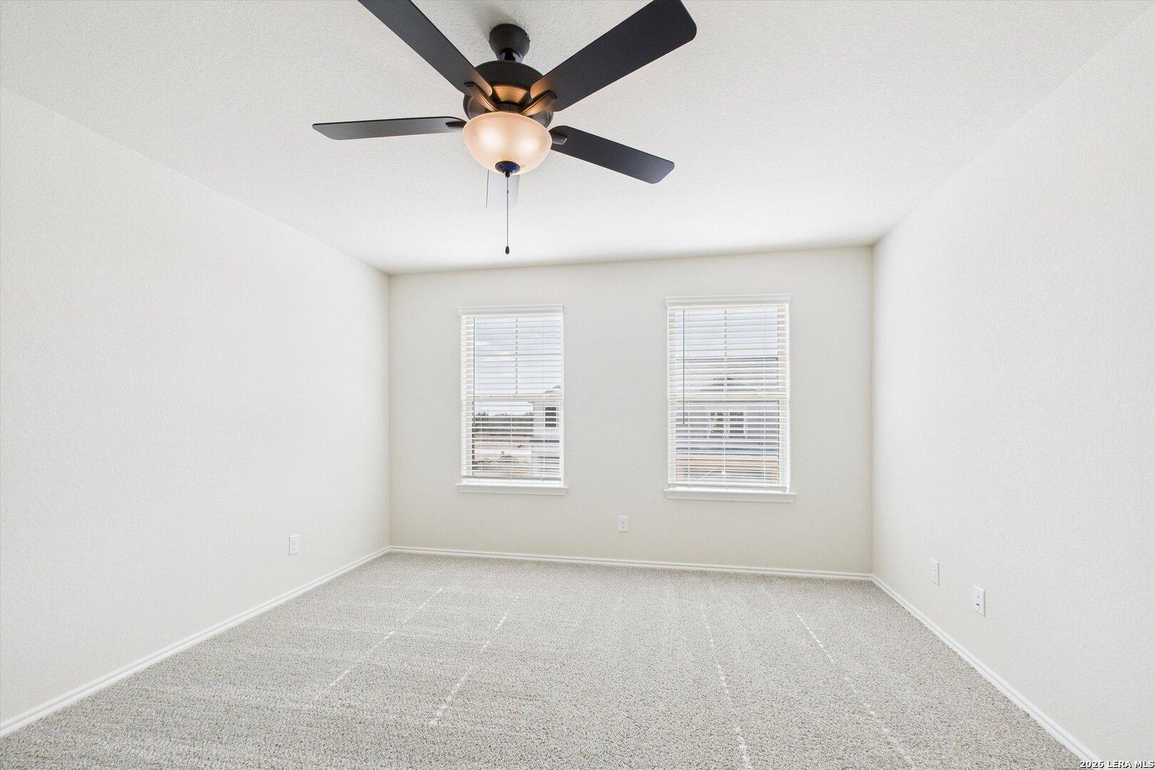 Bright secondary bedroom with ceiling fan, large windows, and carpeted floors in The Gillian B, Davidson Homes, San Antonio, Texas