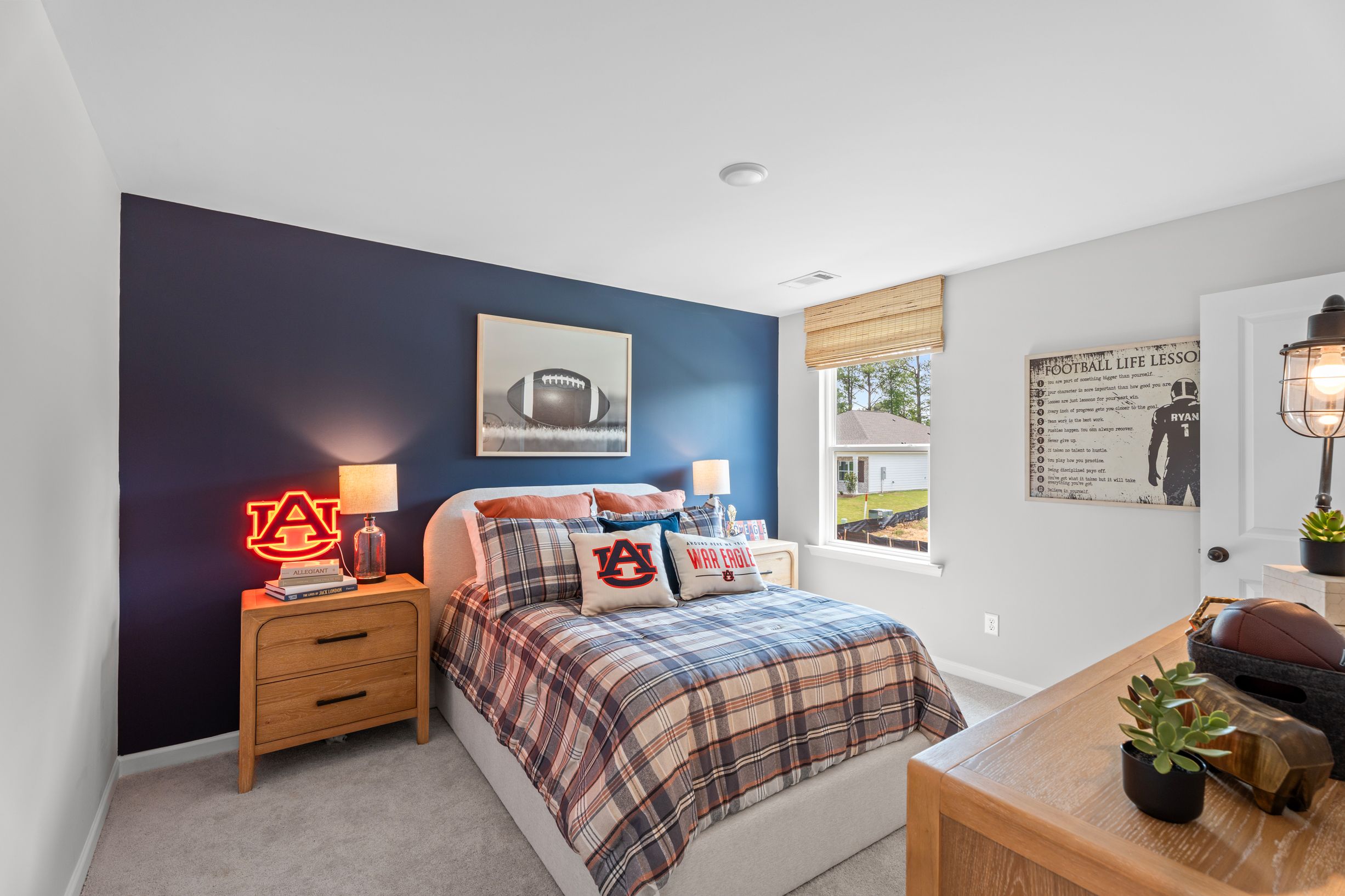 Auburn-themed bedroom at Links Crossing in Auburn, Alabama, featuring navy accent wall, plaid bedding, and sports decor.