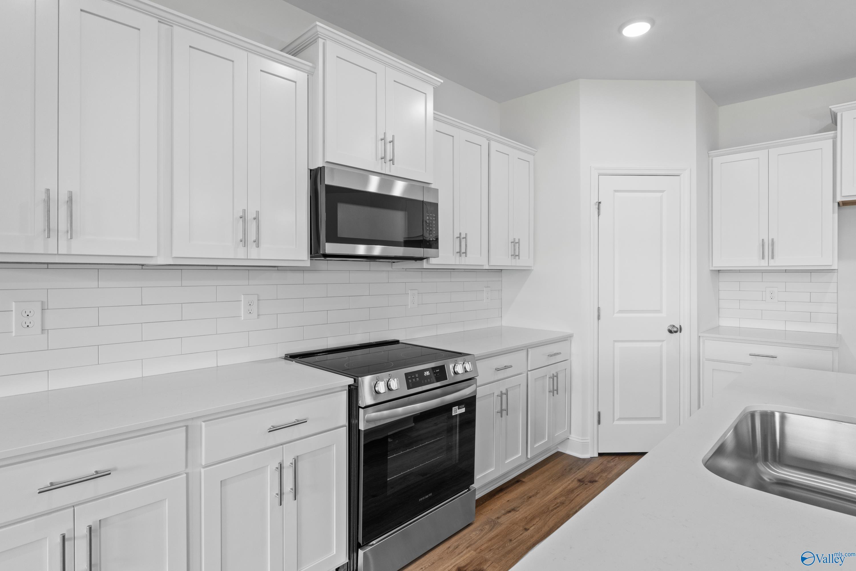 Modern white kitchen featuring stainless steel oven, microwave, and cooktop with subway tile backsplash in Davidson Homes The Rockford B, Toney, AL