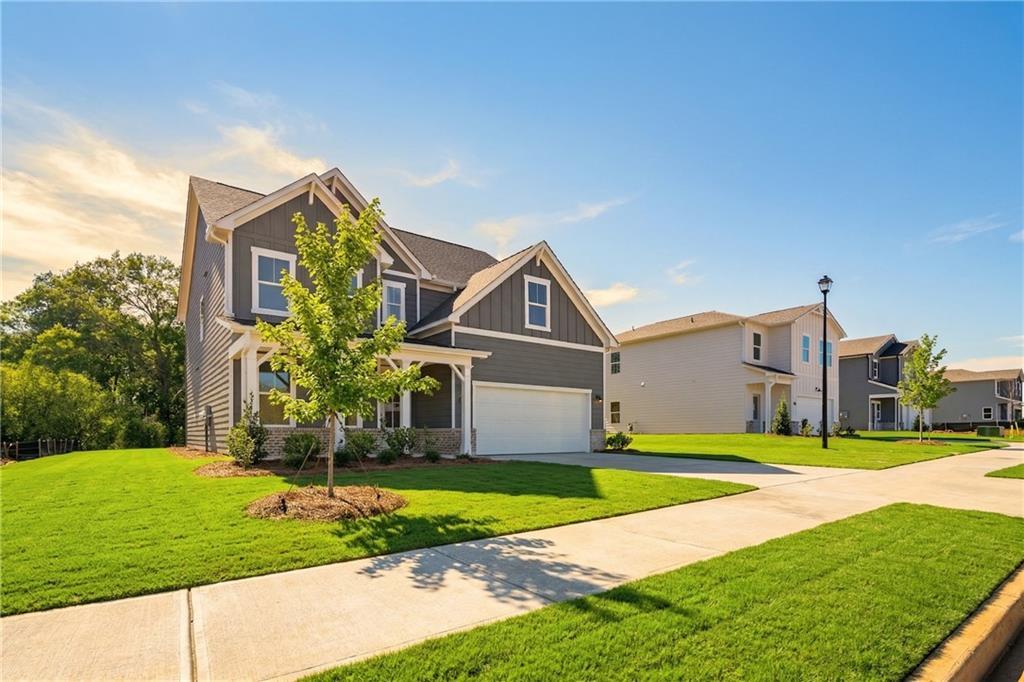 Modern two-story gray home with shingled roof, 2-car garage, lush green lawn, and young tree in Cedar Farms, Winder, Georgia