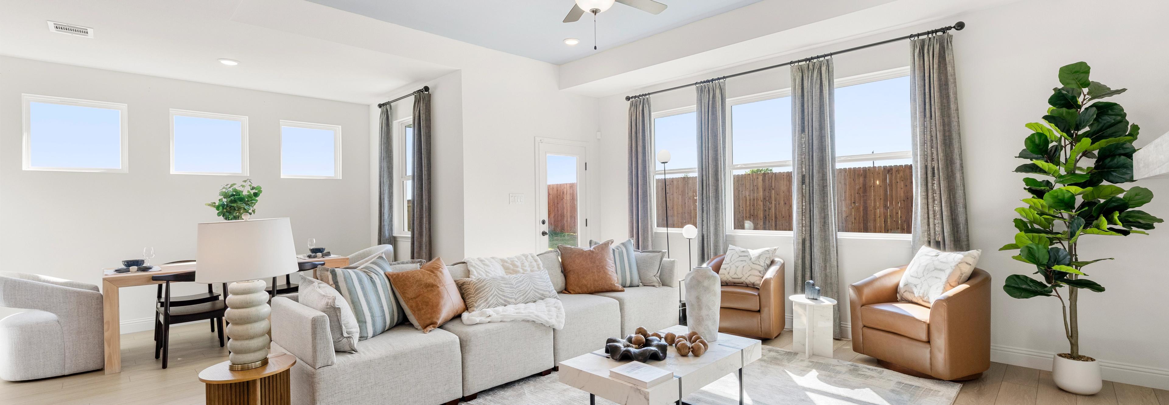 Open-concept living room at Meadow Ridge Estates in Josephine Texas with light wood floors gray sectional sofa ceiling fan and potted plant