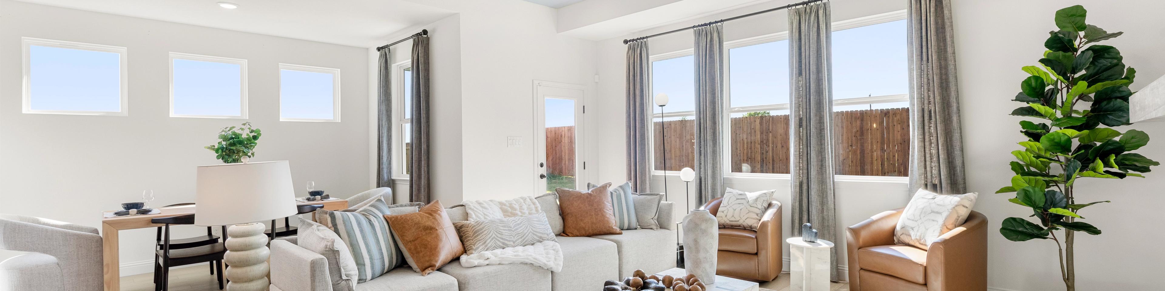 Open-concept living room at Meadow Ridge Estates in Josephine Texas with light wood floors gray sectional sofa ceiling fan and potted plant