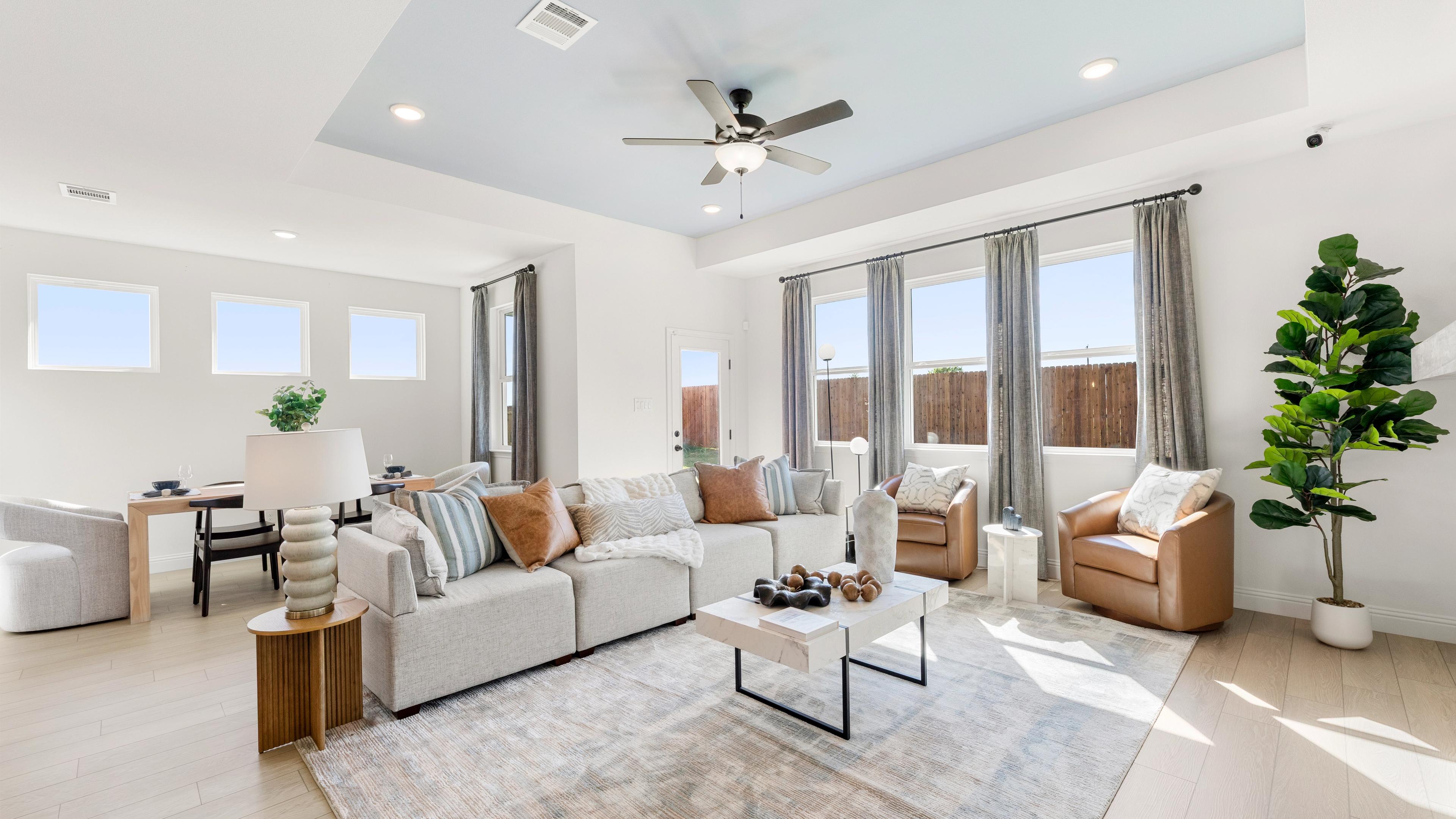 Open-concept living room at Meadow Ridge Estates in Josephine Texas with light wood floors gray sectional sofa ceiling fan and potted plant