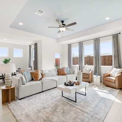 Open-concept living room at Meadow Ridge Estates in Josephine Texas with light wood floors gray sectional sofa ceiling fan and potted plant