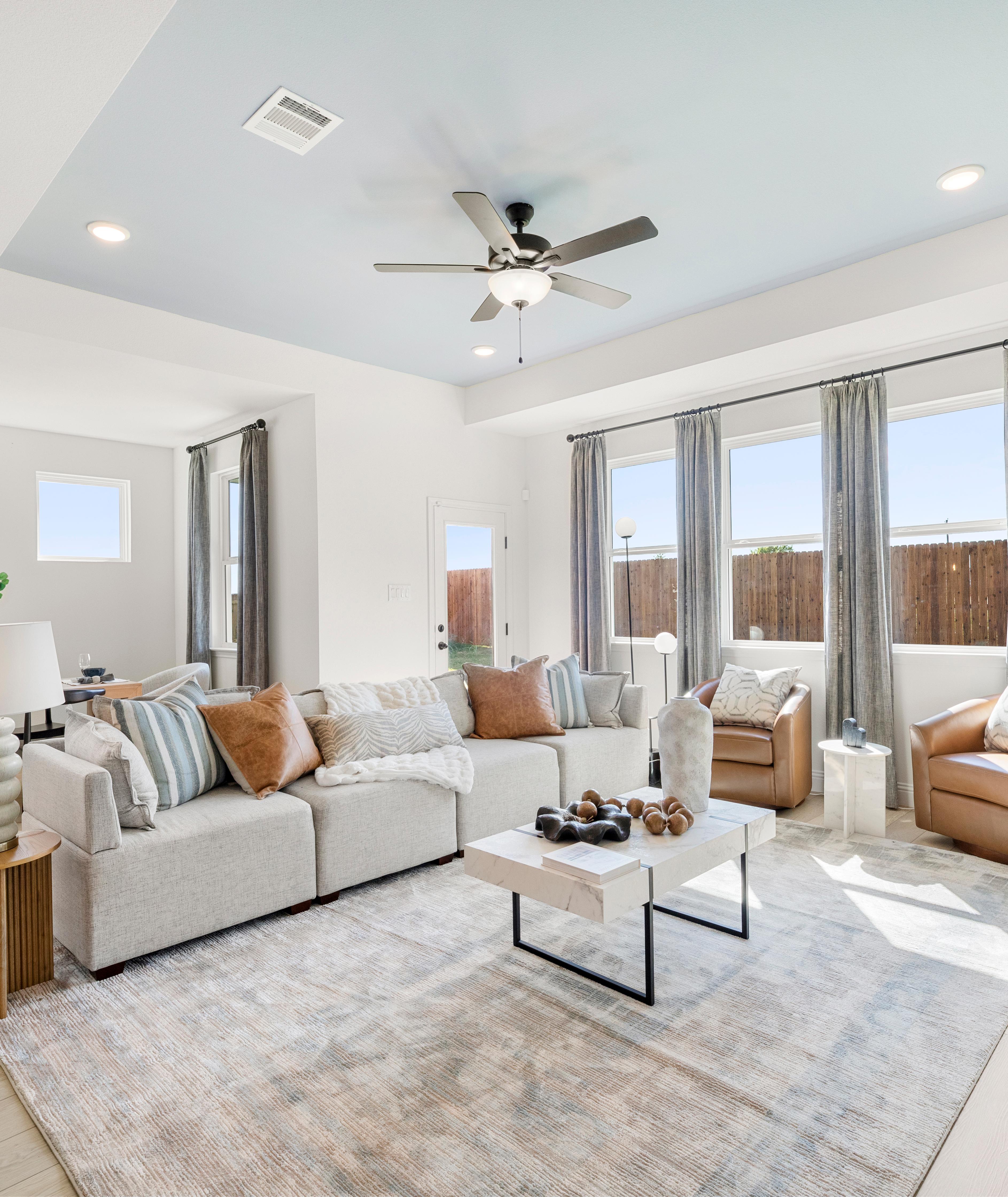 Open-concept living room at Meadow Ridge Estates in Josephine Texas with light wood floors gray sectional sofa ceiling fan and potted plant