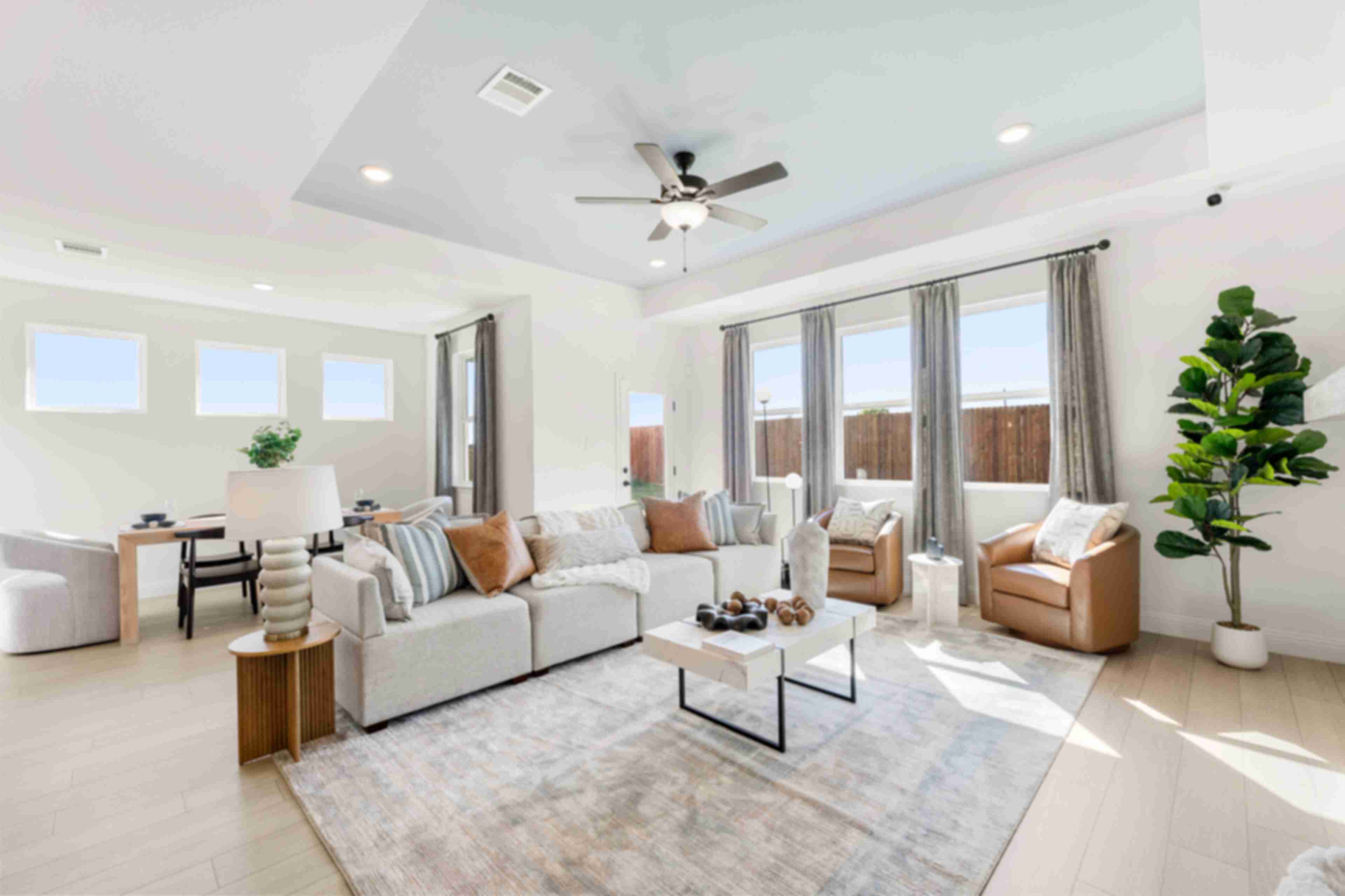 Open-concept living room at Meadow Ridge Estates in Josephine Texas with light wood floors gray sectional sofa ceiling fan and potted plant