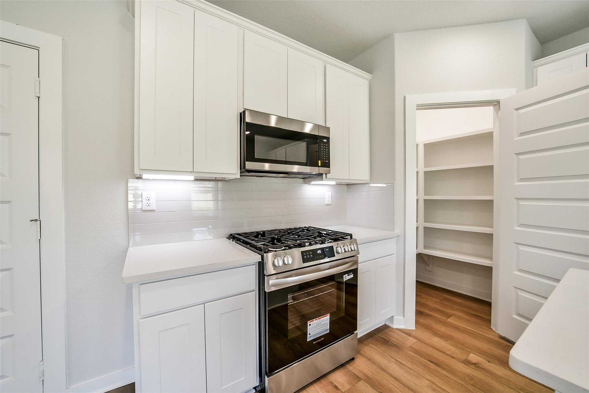 Modern white kitchen featuring stainless steel gas range, microwave, and subway tile backsplash in Davidson Homes The Trinity F, Magnolia, TX