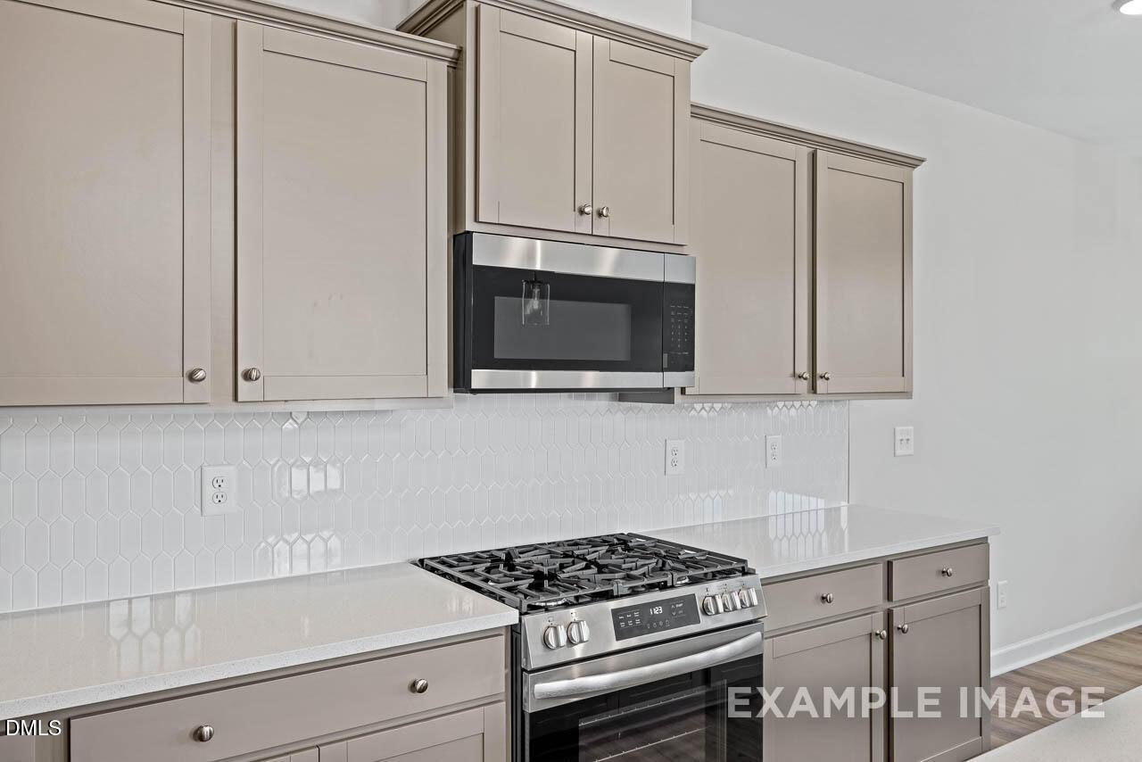 Modern kitchen with gray cabinets, white quartz countertops, and stainless steel appliances in Springvale, Fuquay-Varina home.