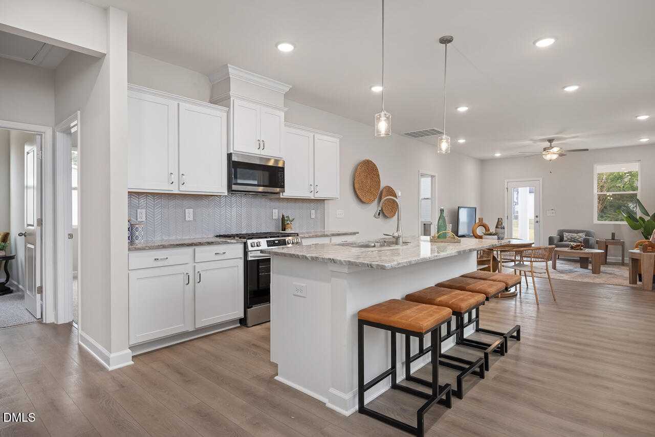 Open-concept kitchen with white shaker cabinets, stainless steel appliances, quartz island and bar stools in The Carter C by Davidson Homes, Lillington, NC
