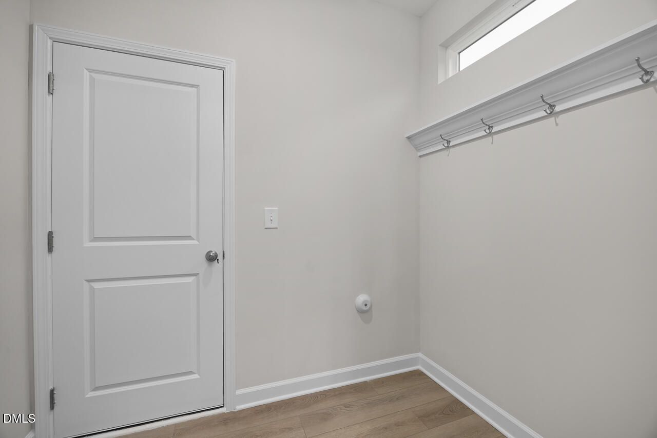 Functional mudroom with white entry door, coat hooks, and storage shelf in Davidson Homes The Gavin B, Gregory Village, Lillington, NC