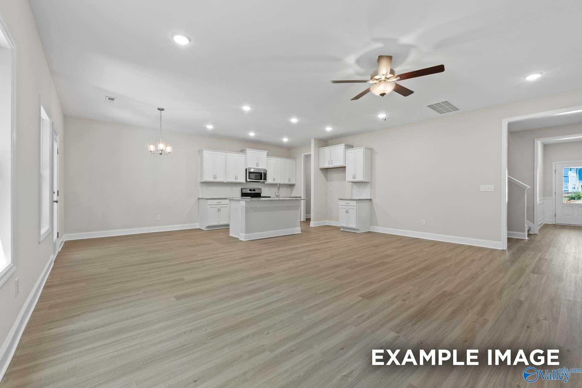 Open-concept kitchen and great room with white cabinets, center island, hardwood floors, ceiling fan in The Camden C home, Huntsville, AL