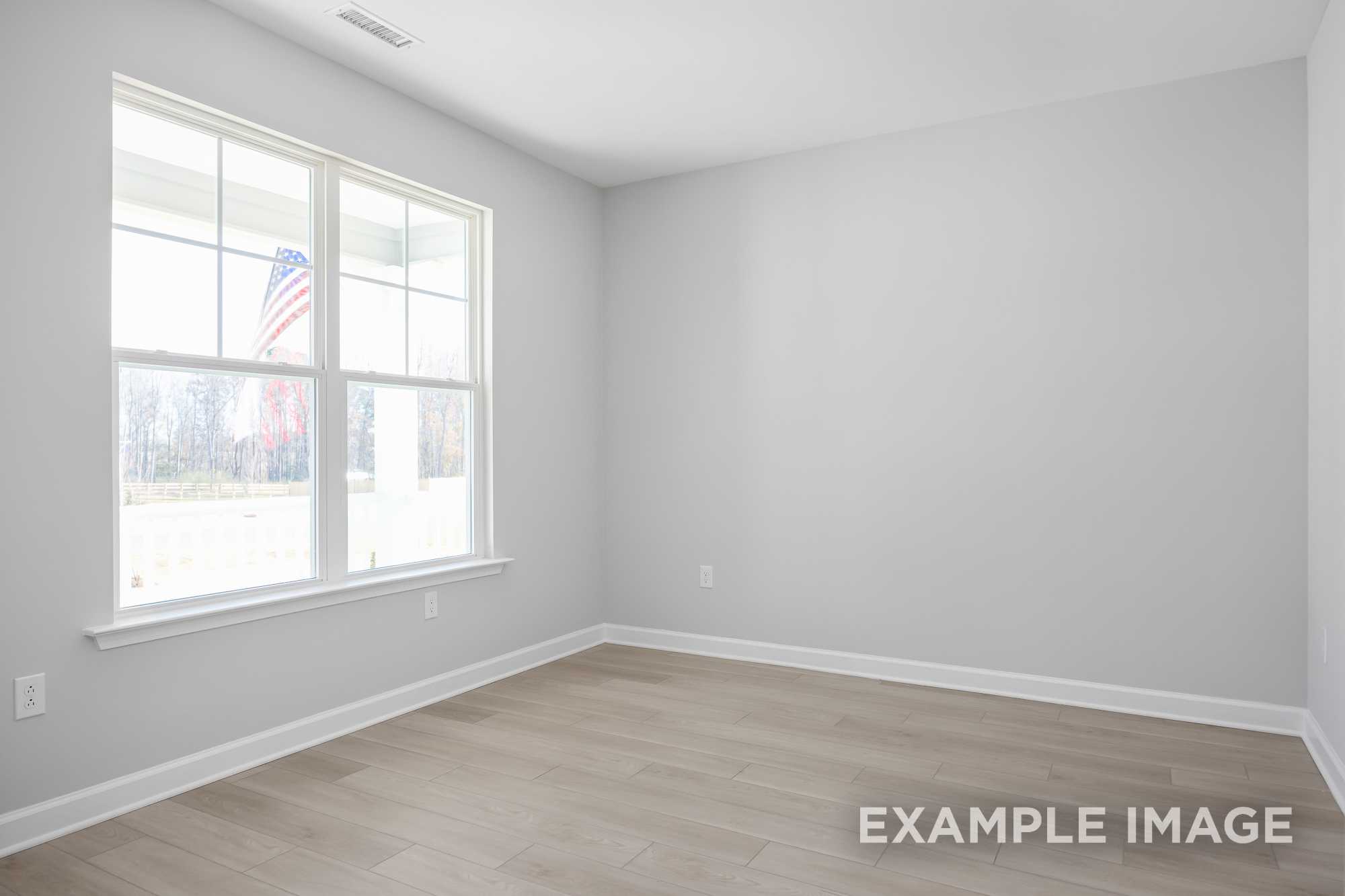 Empty upstairs bedroom in The Cypress D II by Davidson Homes, light gray walls, hardwood floors, large window with American flag view