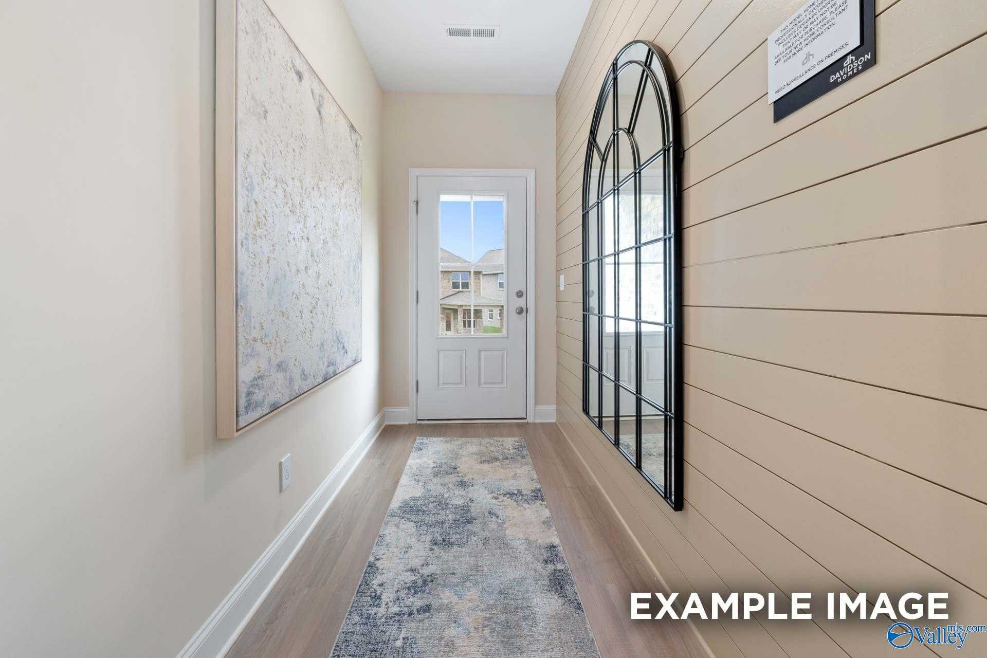 Bright hallway with shiplap walls, arched mirror, hardwood floors, and exterior door in Davidson Homes The Camden B, Huntsville, AL