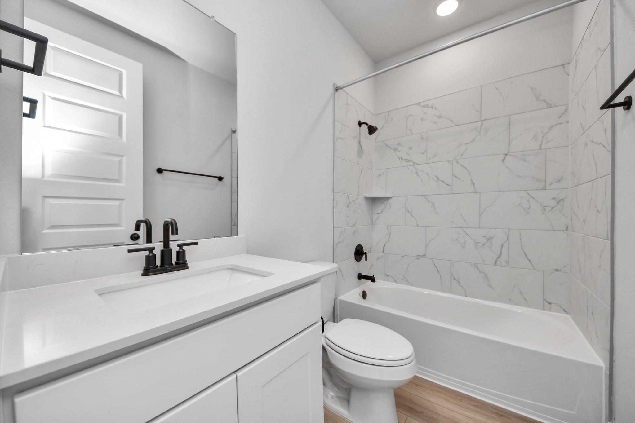 Modern bathroom with white vanity, marble-look tile tub surround, and black fixtures in a Davidson Homes Laguna C floor plan.