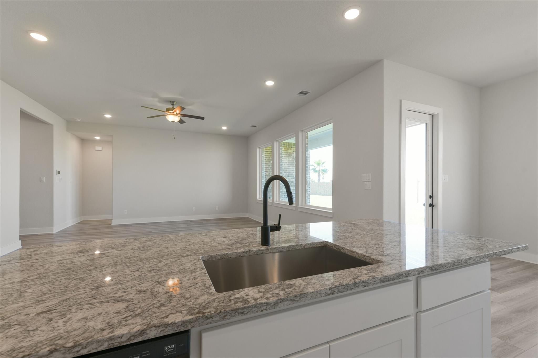 Modern open-concept kitchen with granite island, stainless sink, white cabinets in Davidson Homes The Edward C, Lago Mar, Texas City