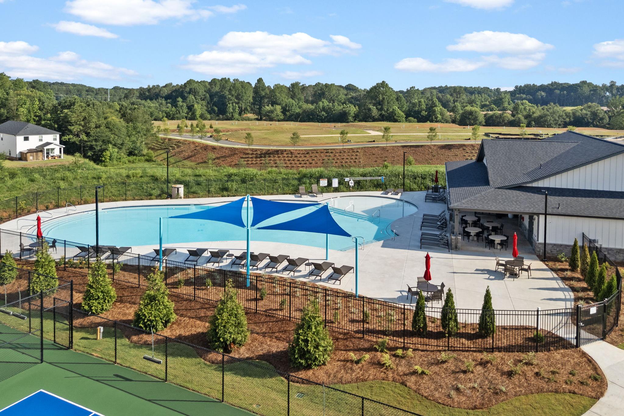 Resort-style swimming pool at Hemingway in Cumming GA with blue shaded umbrellas, lounge chairs, clubhouse, and adjacent tennis court