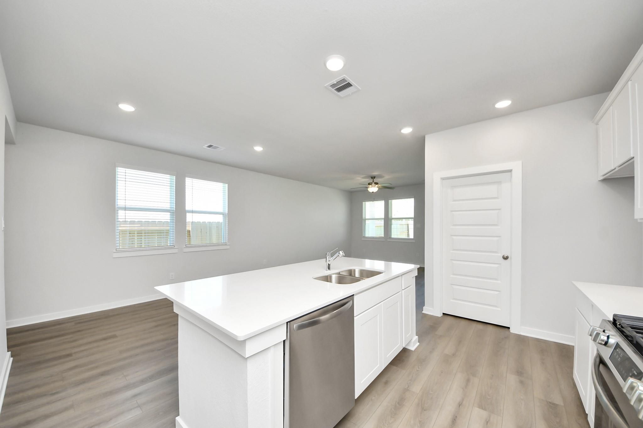 Modern kitchen with white island and stainless appliances in The Costa A floor plan at Emberly in Beasley, Texas.