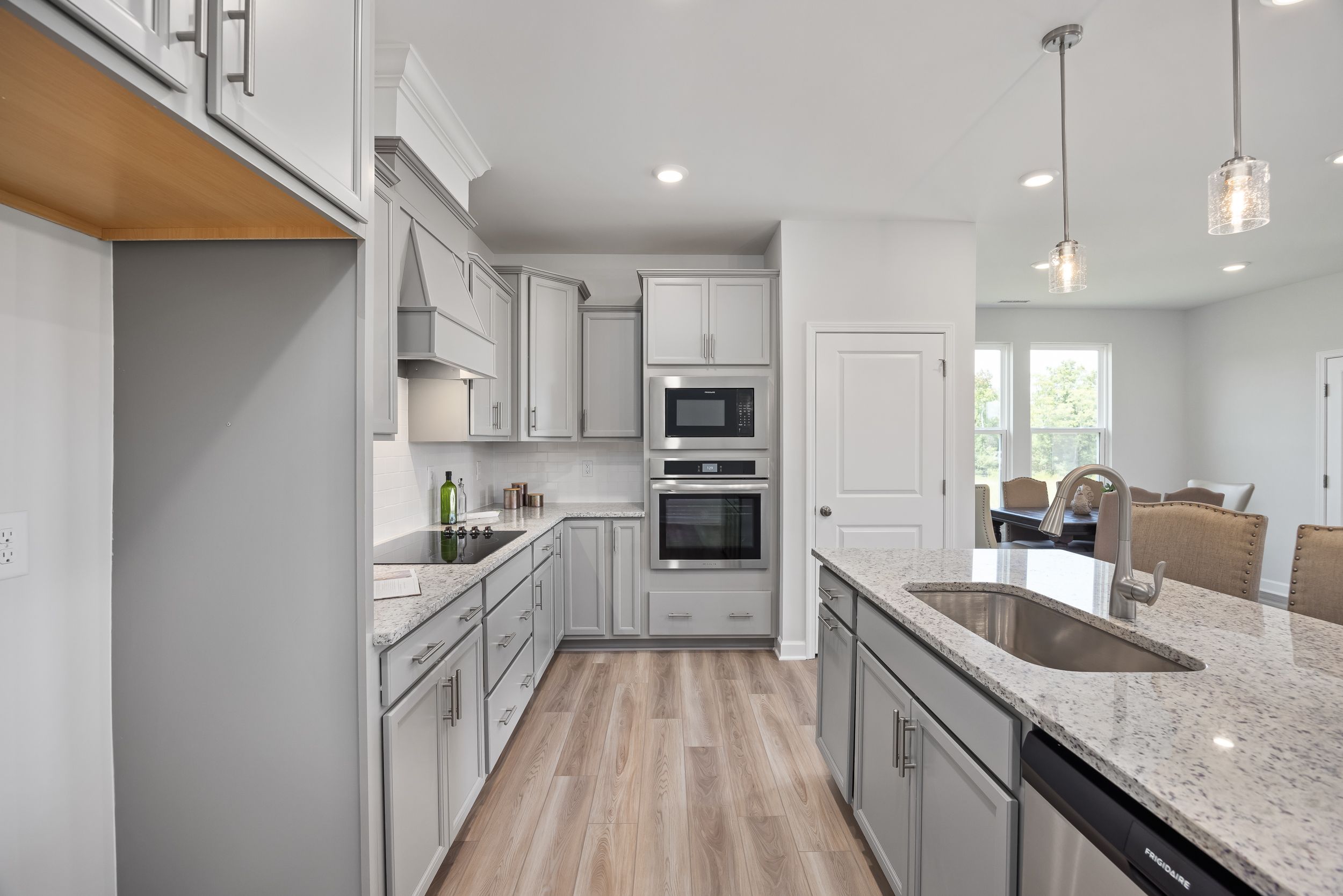 Spacious modern kitchen in The Daphne C with gray shaker cabinets, quartz island sink, double wall ovens, and open dining nook