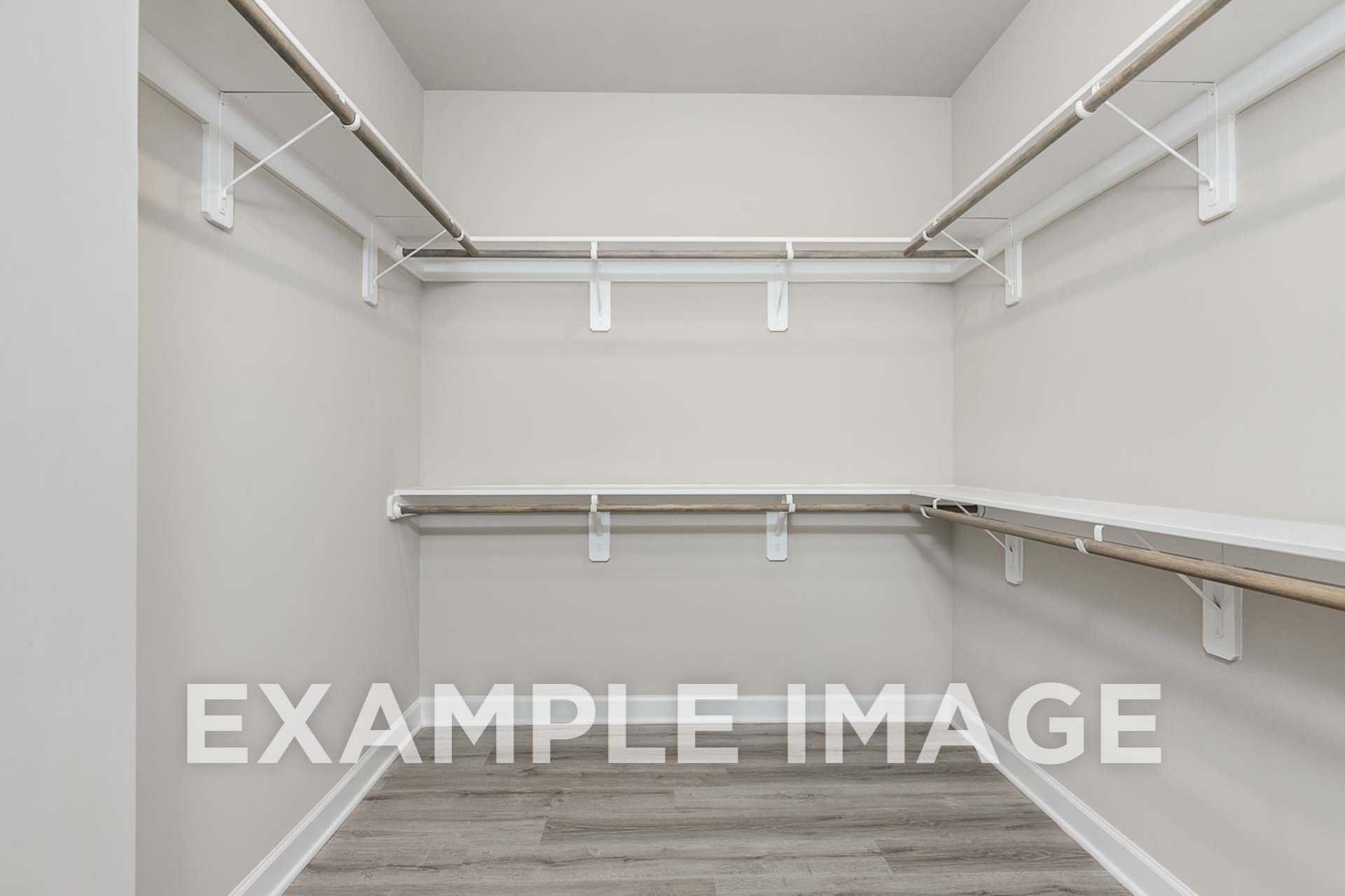Spacious walk-in closet in The Ash E master suite with white walls, laminate flooring, and built-in shelving rods