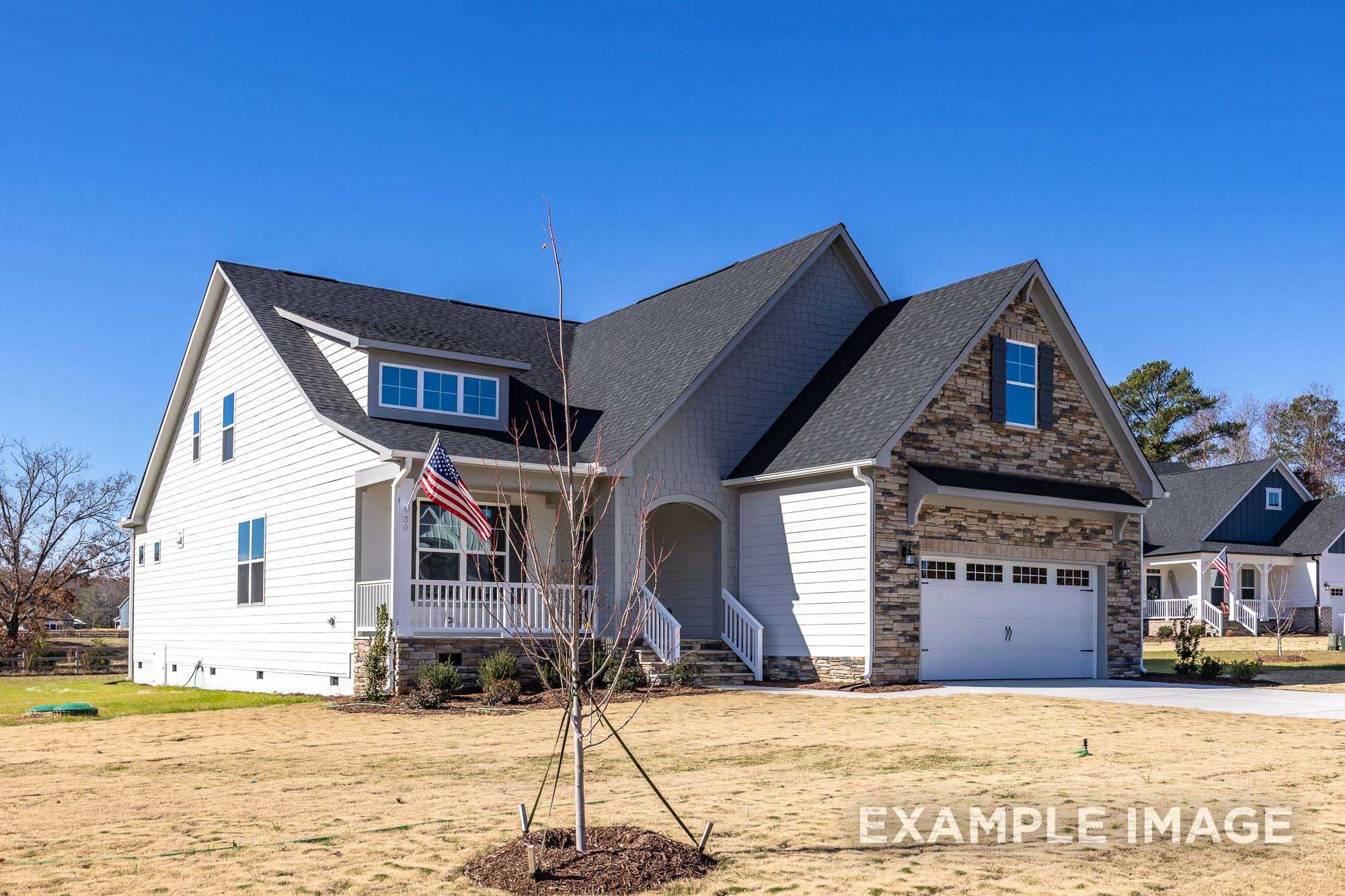 Two-story The Cypress D II home elevation by Davidson Homes with white siding, stone accents, American flag porch, and 2-car garage in Angier NC