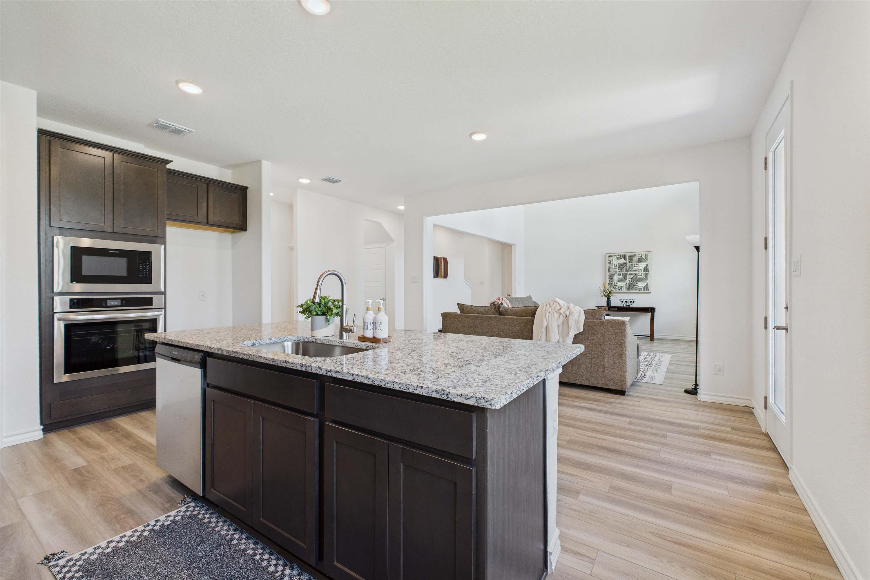Open-concept kitchen in The Danbury featuring granite island, dark cabinetry, and seamless flow into the living area.