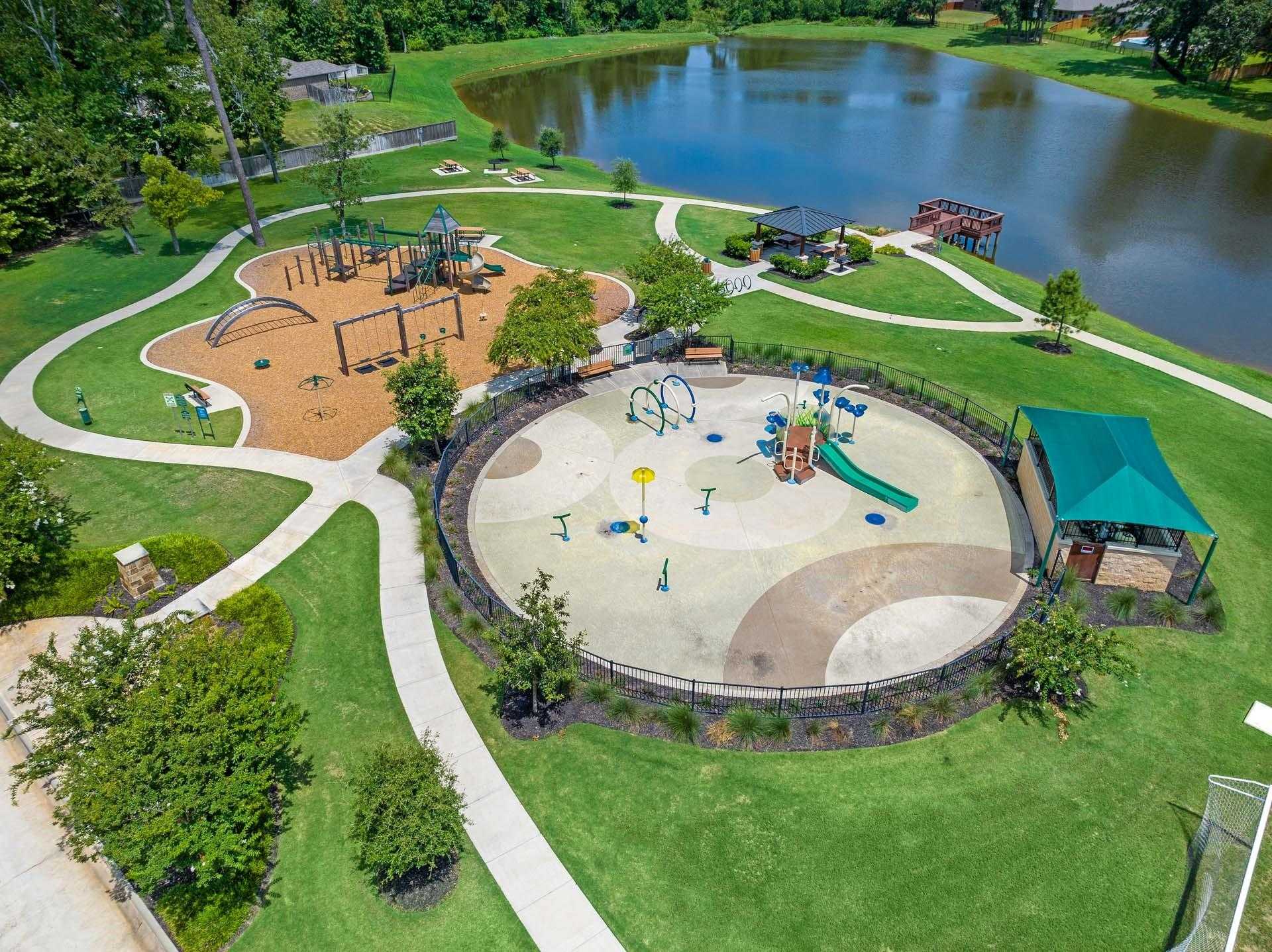 Vibrant playground with slides, swings, climbers amid lush greens, paths, and serene lake in Lakes at Black Oak, Magnolia, Texas