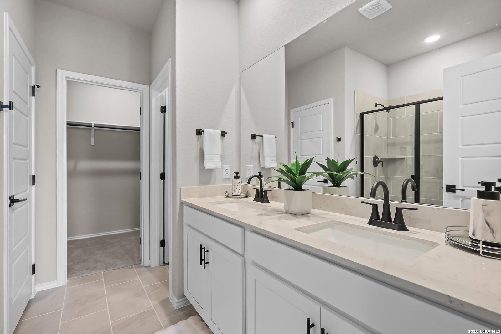 Modern bathroom with double vanity, quartz countertops, and walk-in closet in The Daphne H by Davidson Homes in Seguin, TX.
