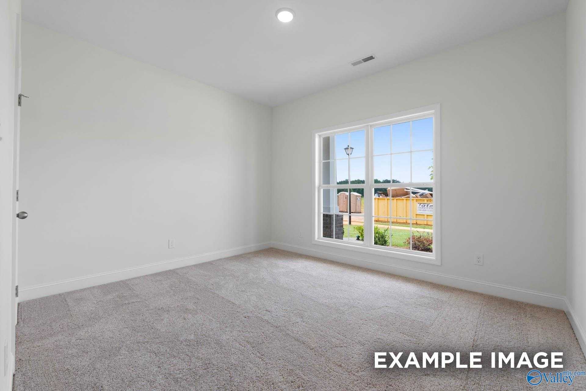 Bright empty bedroom with white walls, beige carpet, and large window overlooking green yard in Davidson Homes The Daphne D, Athens, Alabama