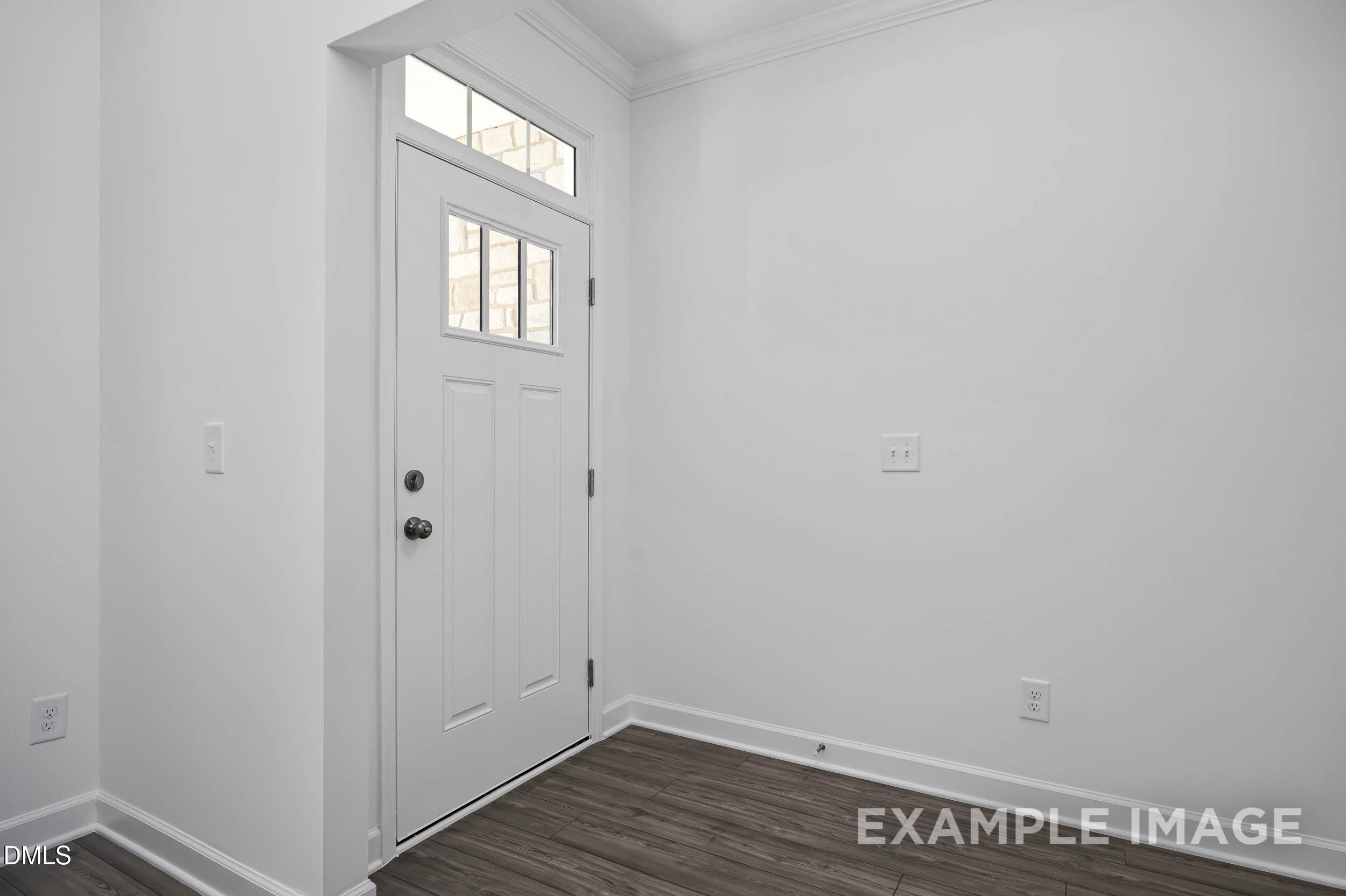 Bright entry foyer with white paneled door, transom window, and hardwood floors in The Willow D, Zebulon, NC