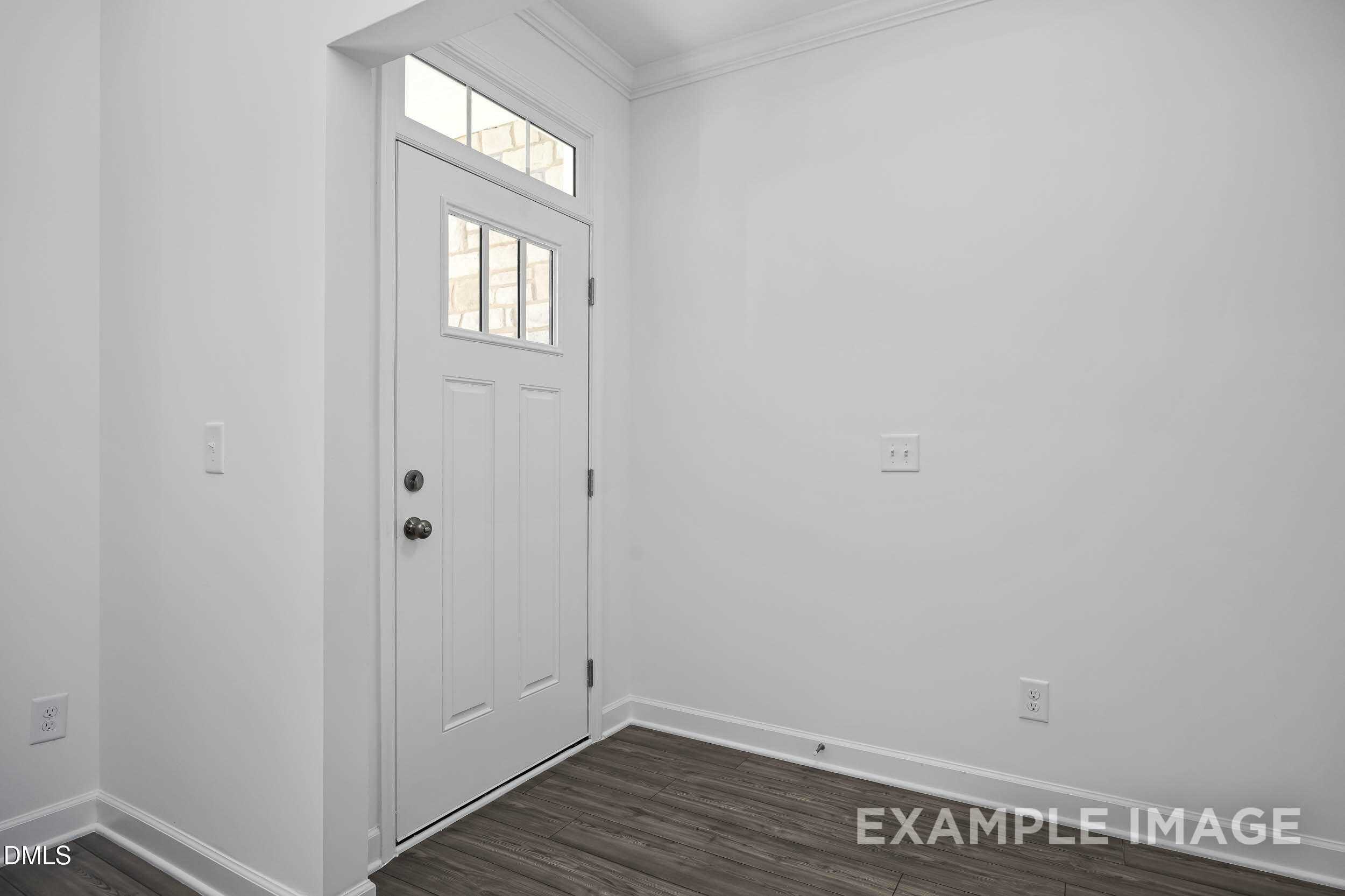 Bright entry foyer with white paneled door, transom window, and hardwood floors in The Willow D, Zebulon, NC