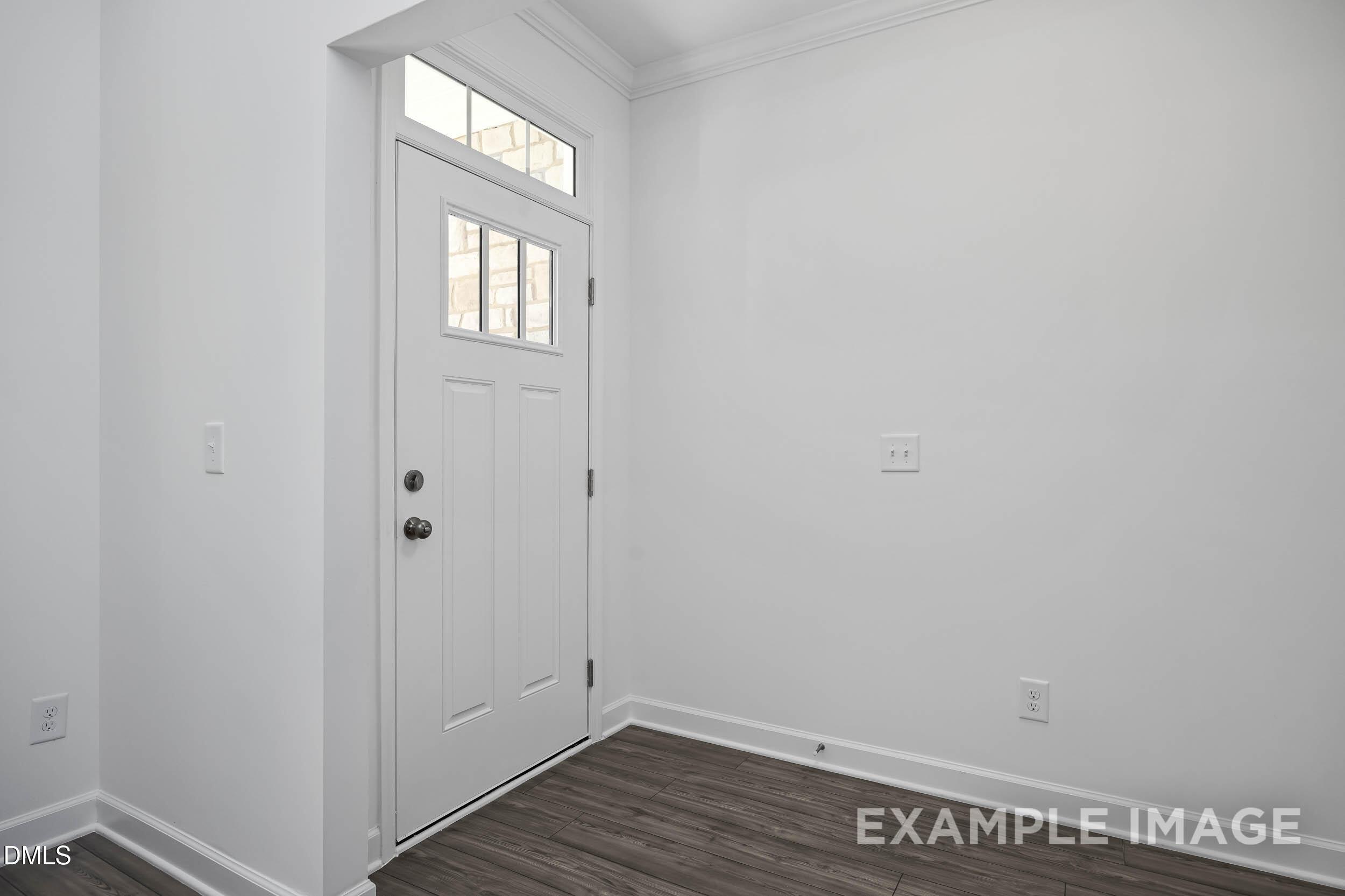 Bright entry foyer with white paneled door, transom window, and hardwood floors in Davidson Homes The Willow D, Zebulon