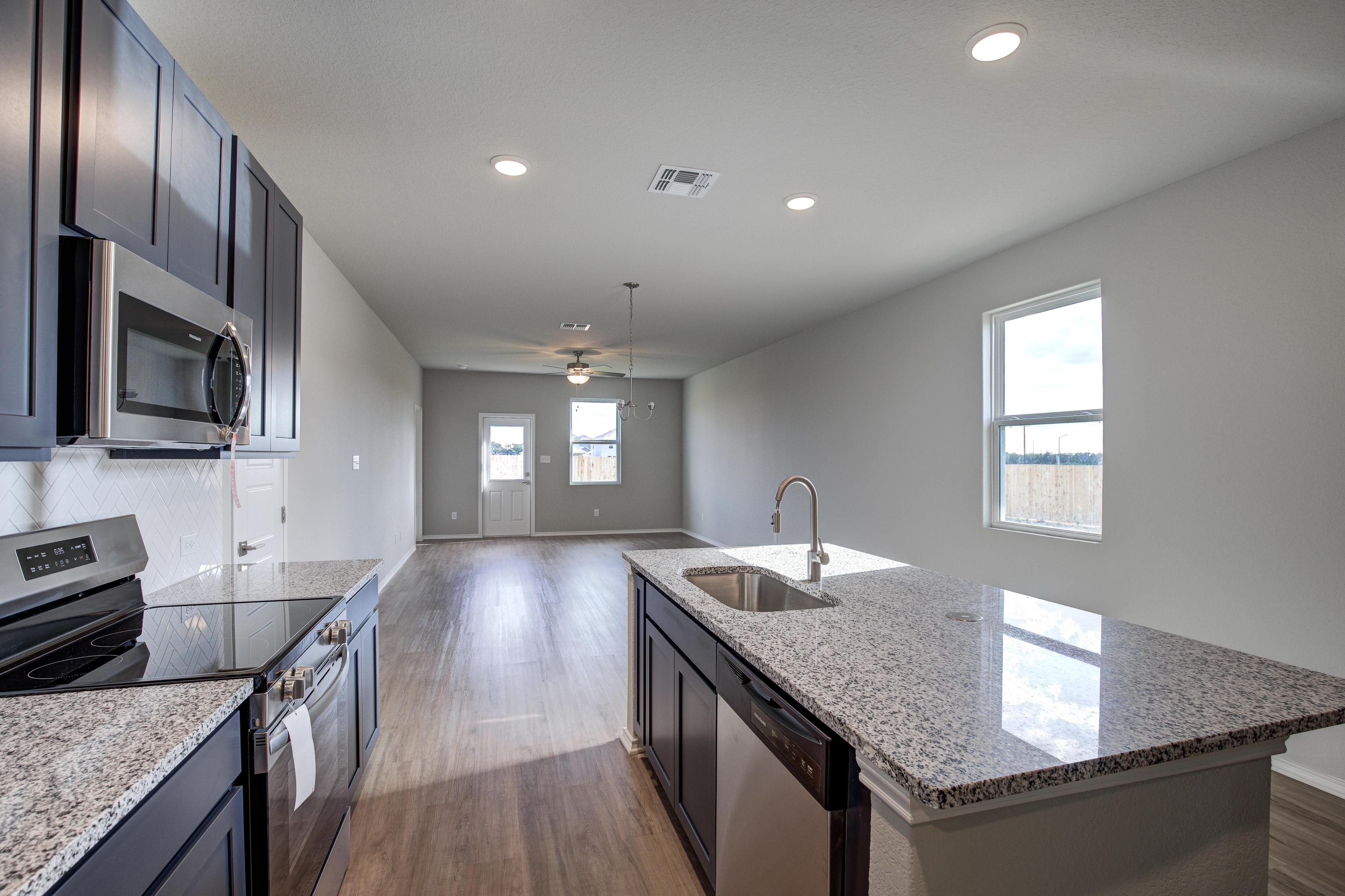 Spacious open-concept kitchen in The Frio D with dark cabinets, granite island, stainless appliances, hardwood floors