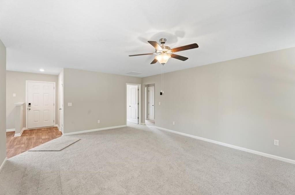 Spacious open living room with beige walls, ceiling fan, and carpeted floors in Davidson Homes The Washington, Phenix City, AL