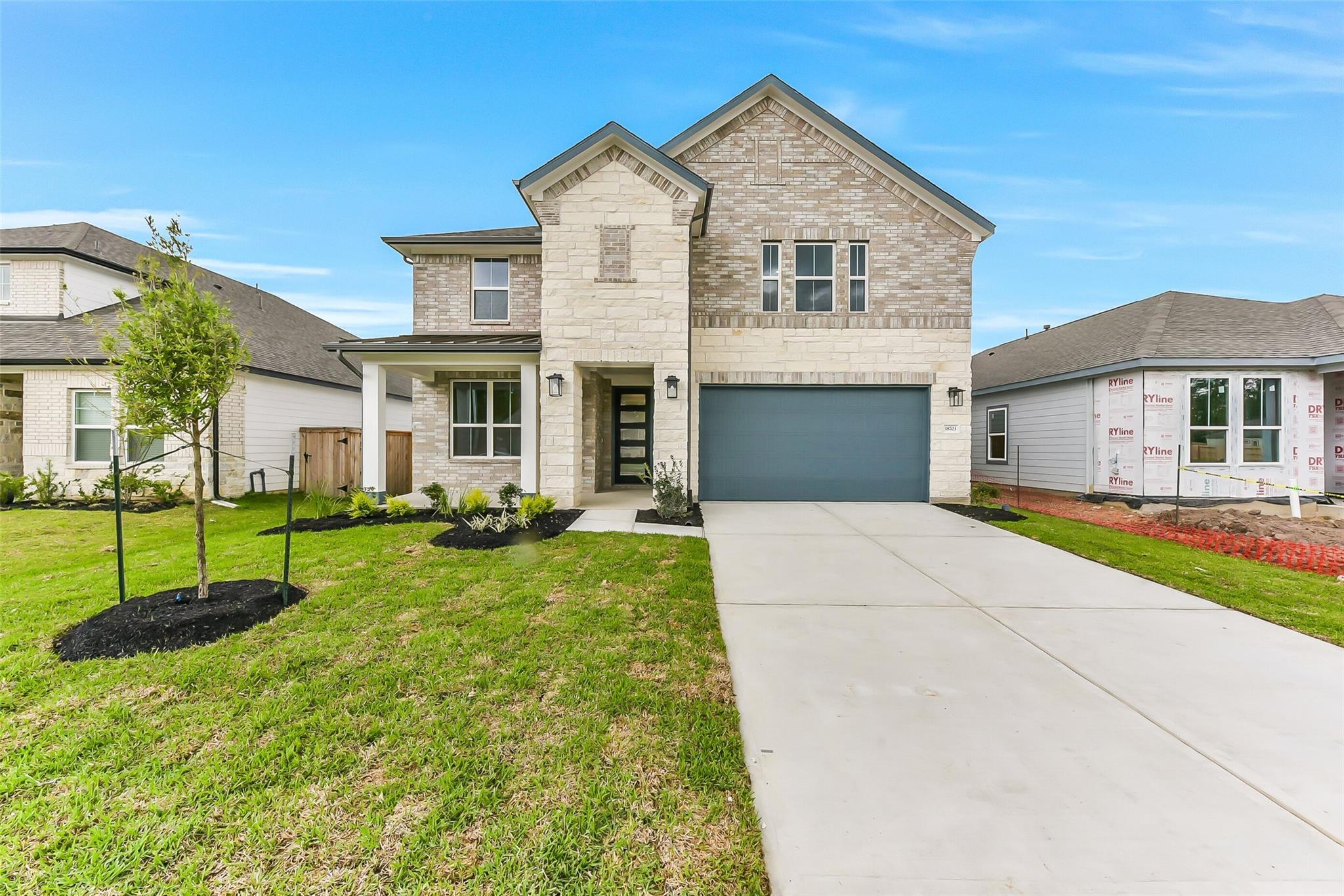 Two-story brick home with stone accents, gray 2-car garage, front porch, landscaped yard in Sundance Cove, Crosby Texas - Davidson Homes Sequoia C