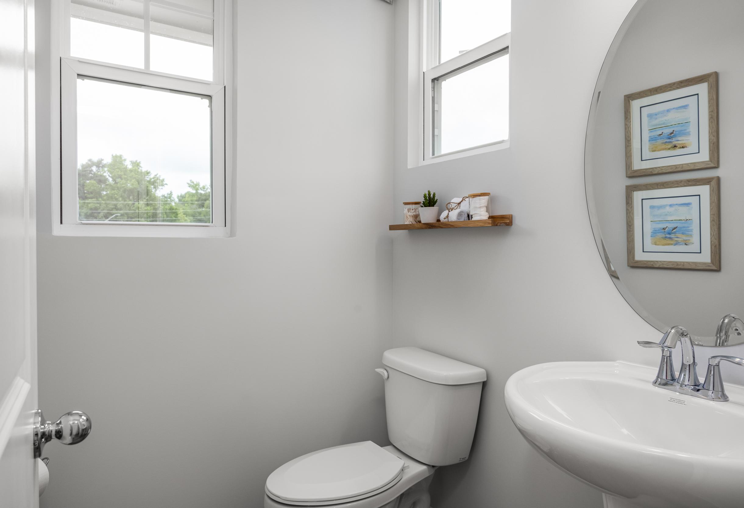 Modern powder room in The Graham featuring a pedestal sink, round mirror, and floating shelf in a Fuquay-Varina home.