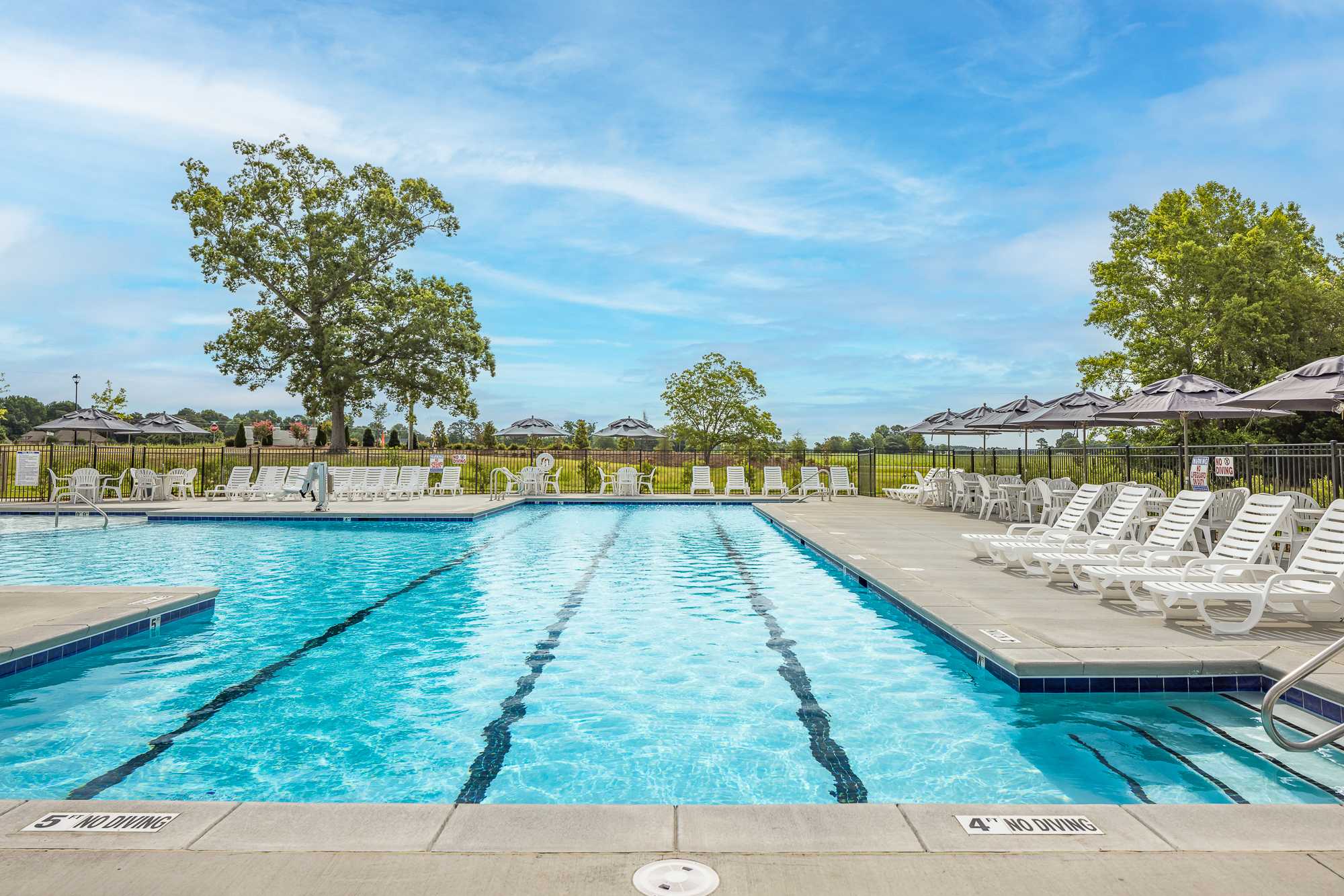Resort-style lap pool at Beverly Place in Four Oaks, NC with lounge chairs, umbrellas, and oak trees