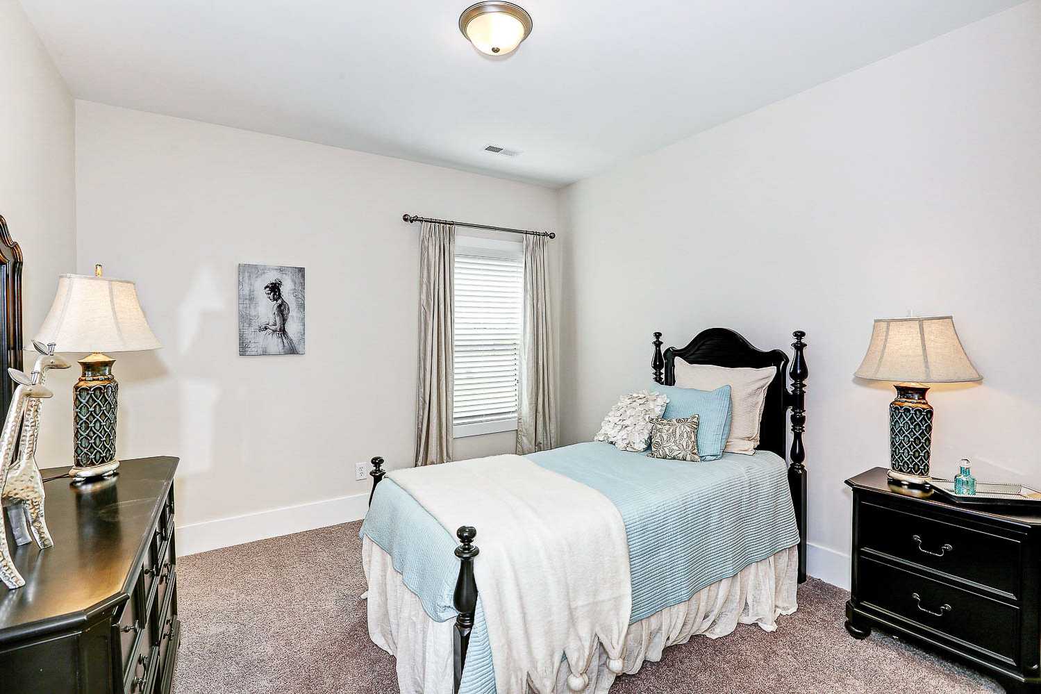Cozy secondary bedroom in The Finleigh featuring twin bed with blue bedding, black wooden furniture, and soft window lighting