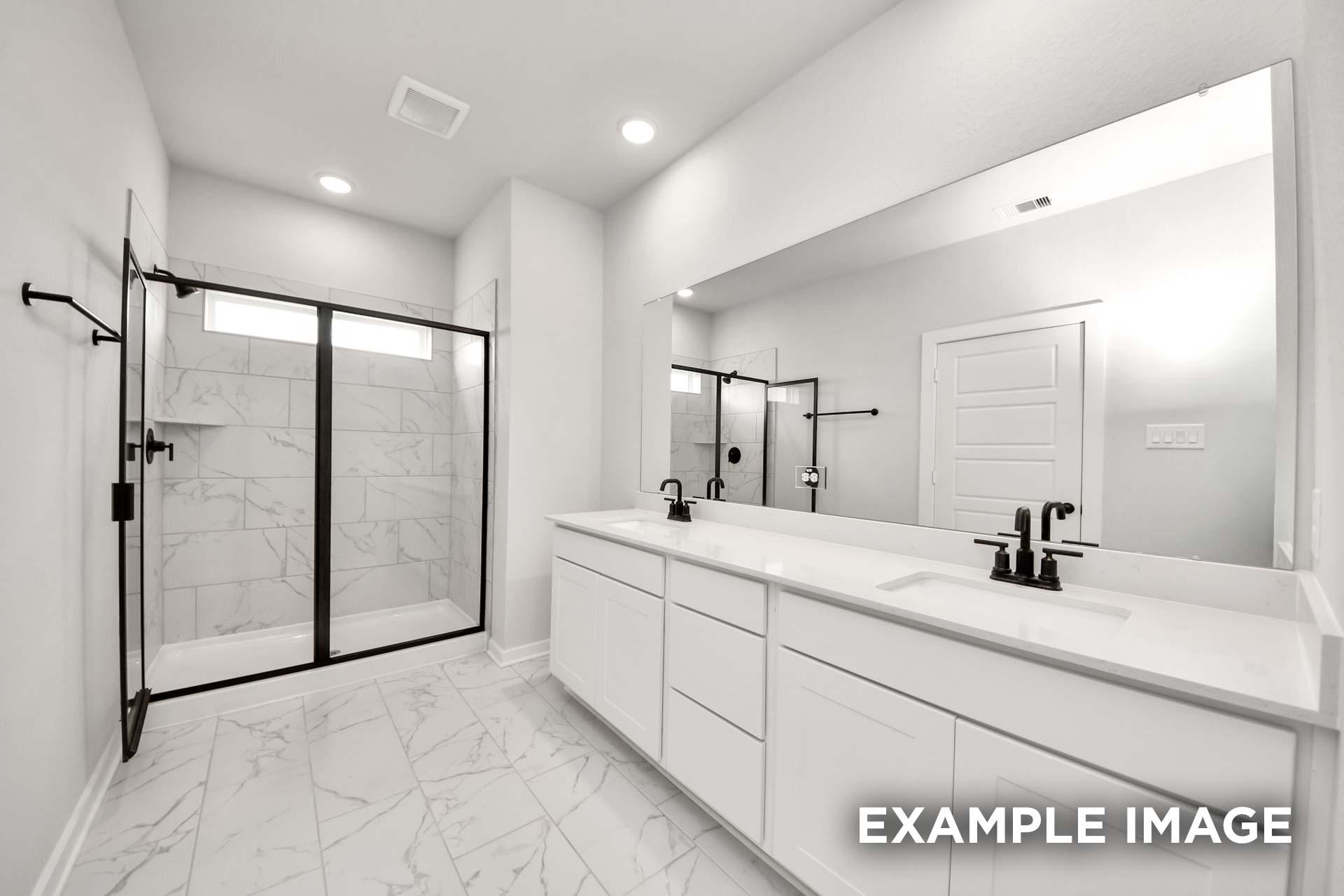 Modern master bathroom in The Sorrento featuring a white dual vanity, marble-style tile, and glass-enclosed walk-in shower.