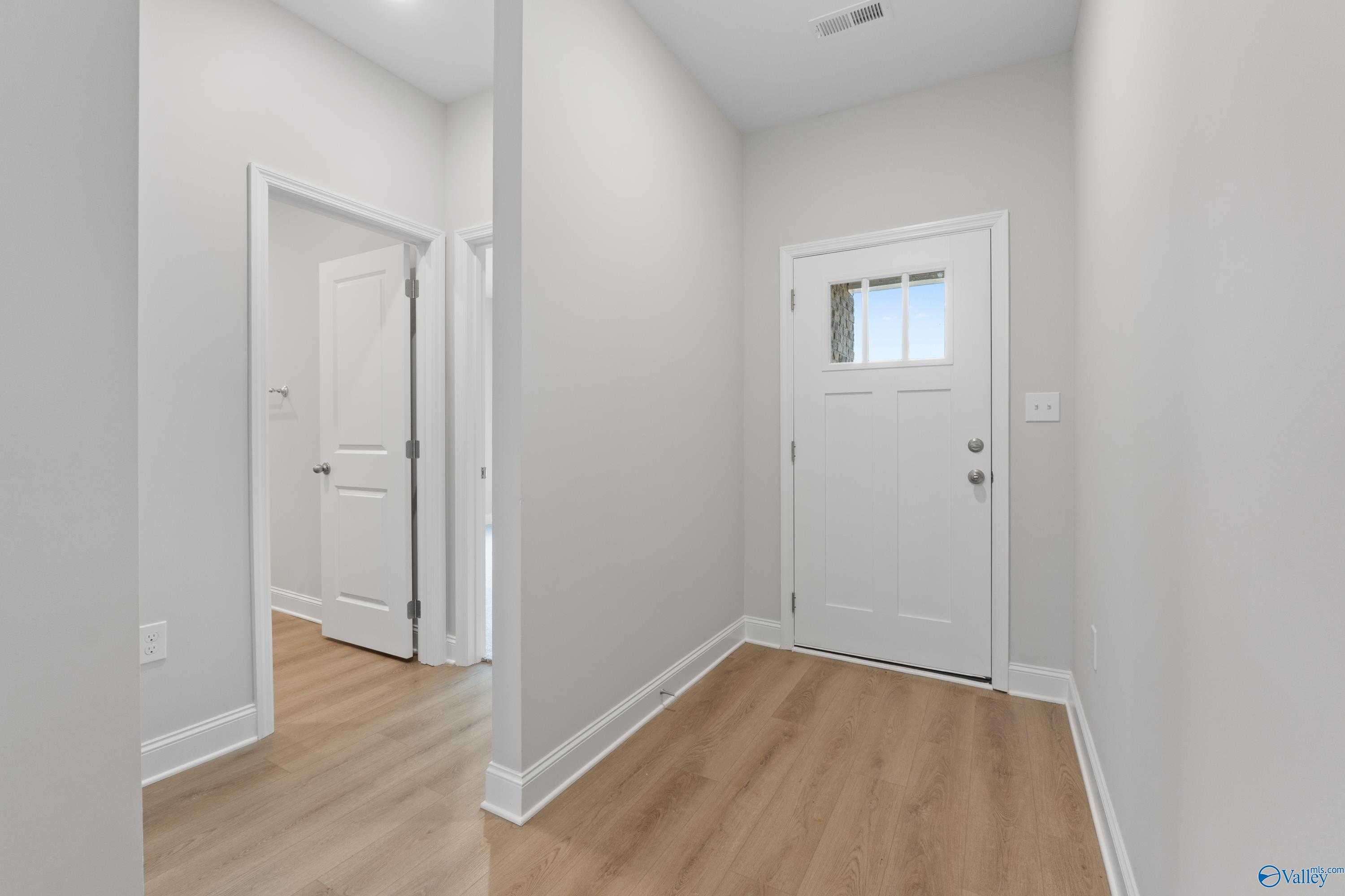 Bright entry foyer with white front door, open bedroom doors, and hardwood floors in Davidson Homes The Asheville C, Huntsville AL
