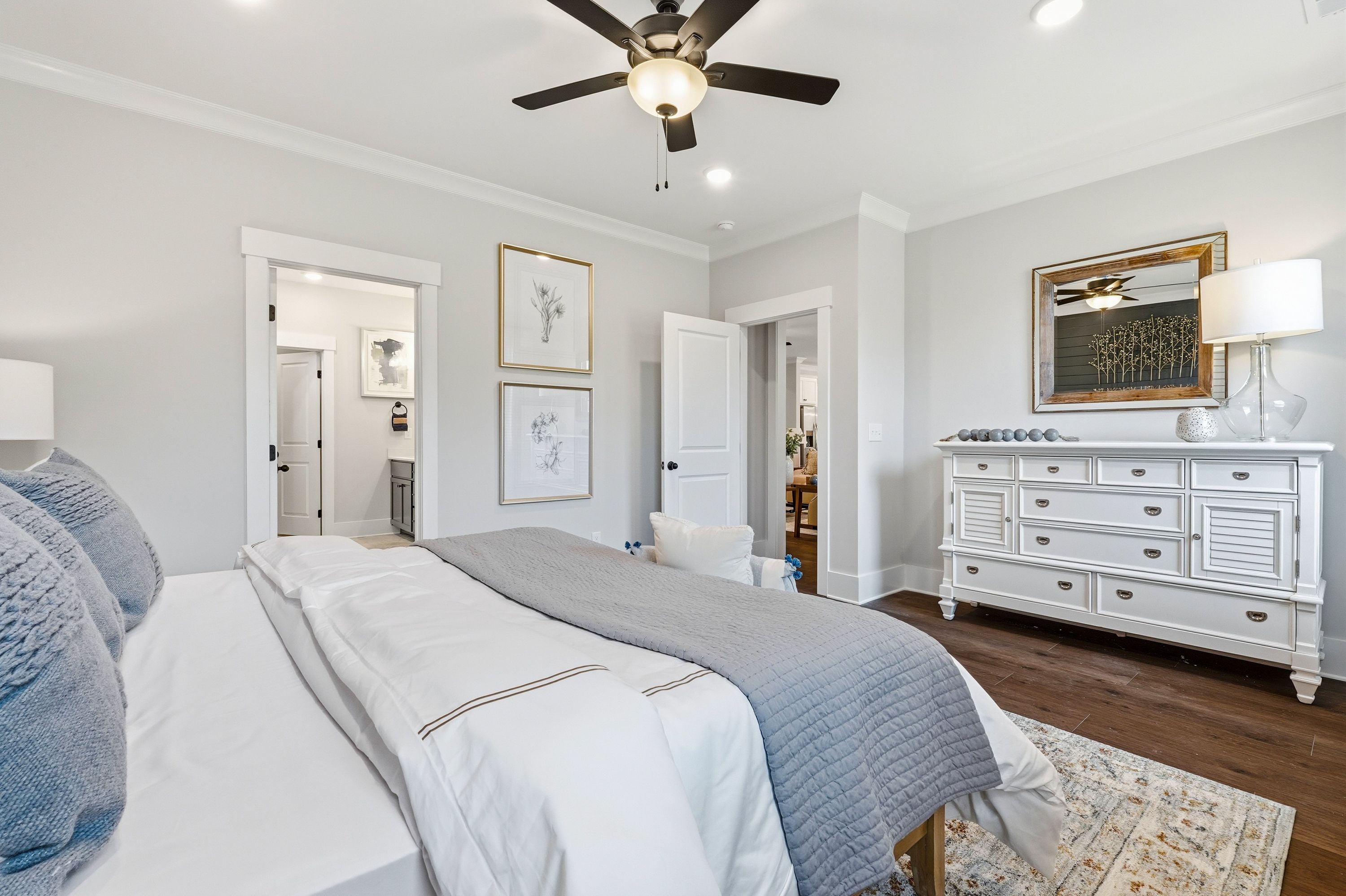 Spacious primary bedroom at Noble Ridge in Cullman Alabama with king bed, gray bedding, white dresser, ceiling fan, and hardwood floors