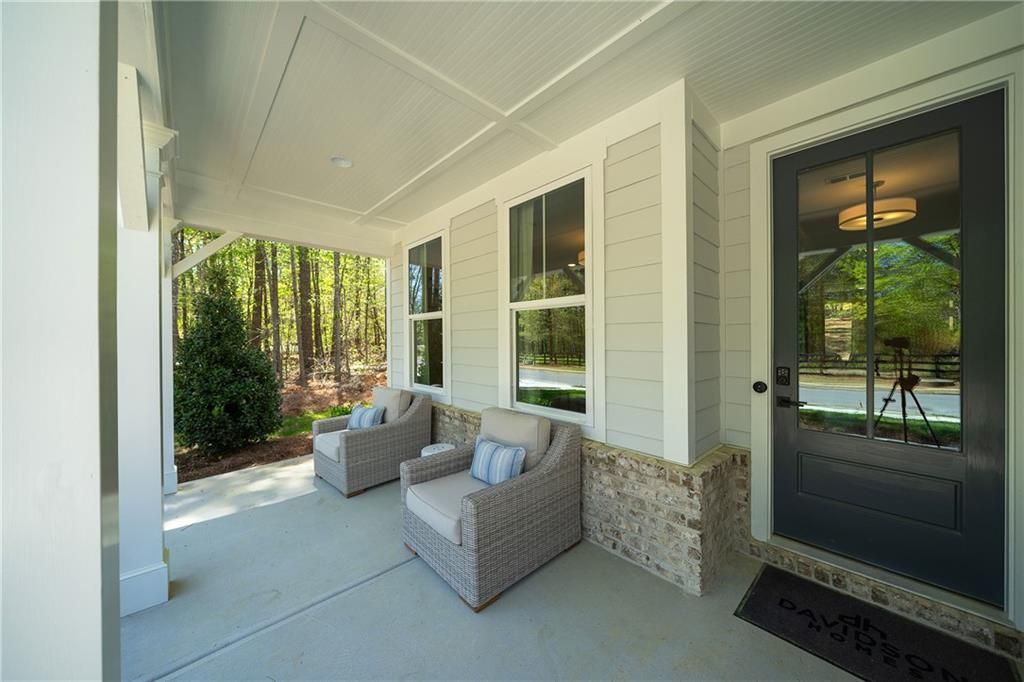 Inviting covered front porch with wicker chairs, stone accents, and wooded views on Davidson Homes The Willow B in Riverwood, Dallas, Georgia