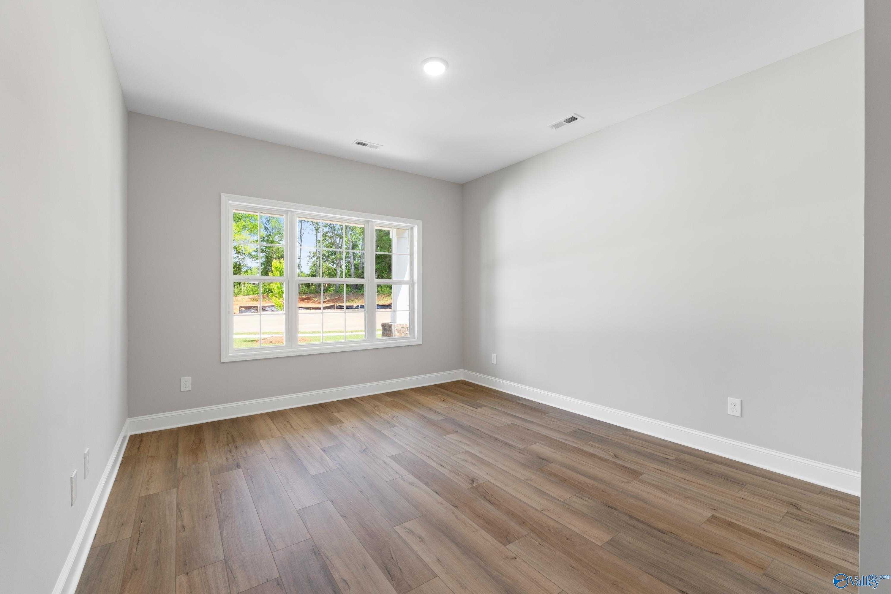 Bright bedroom with gray walls, large windows overlooking greenery, and hardwood floors in Davidson Homes The Chelsea B, New Market, Alabama