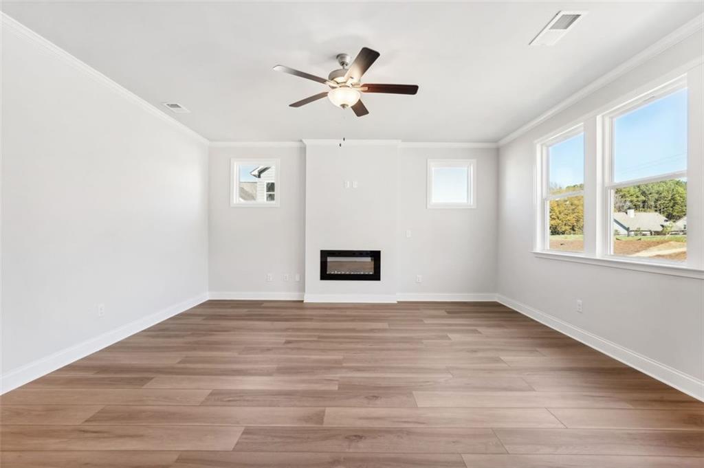 Bright living room with modern fireplace, ceiling fan, and wood-style flooring in The Hickory C home, Wehunt Meadows.