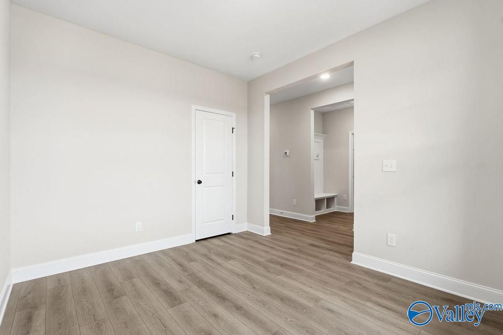 Bright bedroom with white door, neutral walls, and wood flooring opening to laundry area with built-in bench in Davidson Homes Rockford B, Hartselle AL