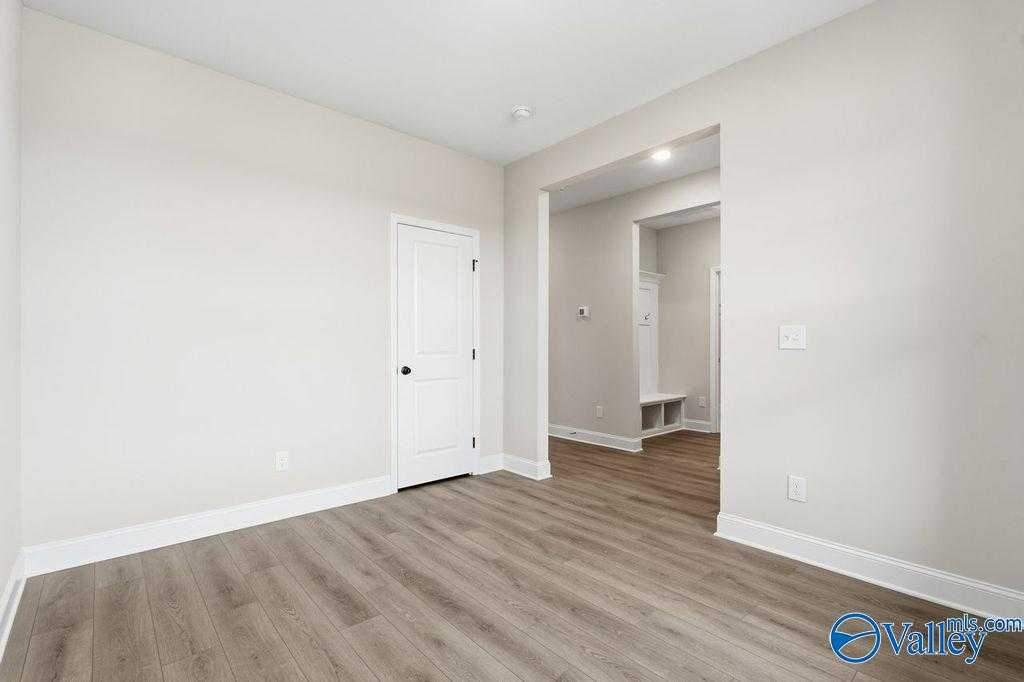 Bright bedroom with white door, neutral walls, and wood flooring opening to laundry area with built-in bench in Davidson Homes Rockford B, Hartselle AL