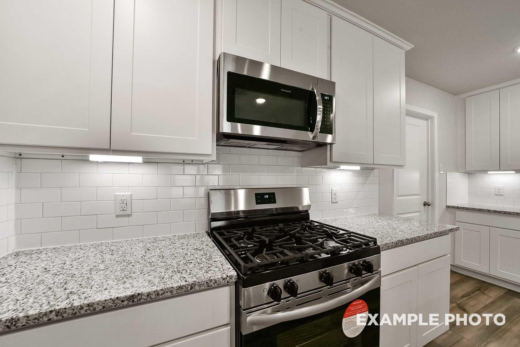 Bright kitchen with white cabinets, granite countertops, stainless steel gas range and microwave in Davidson Homes Tierra B, Beasley, Texas