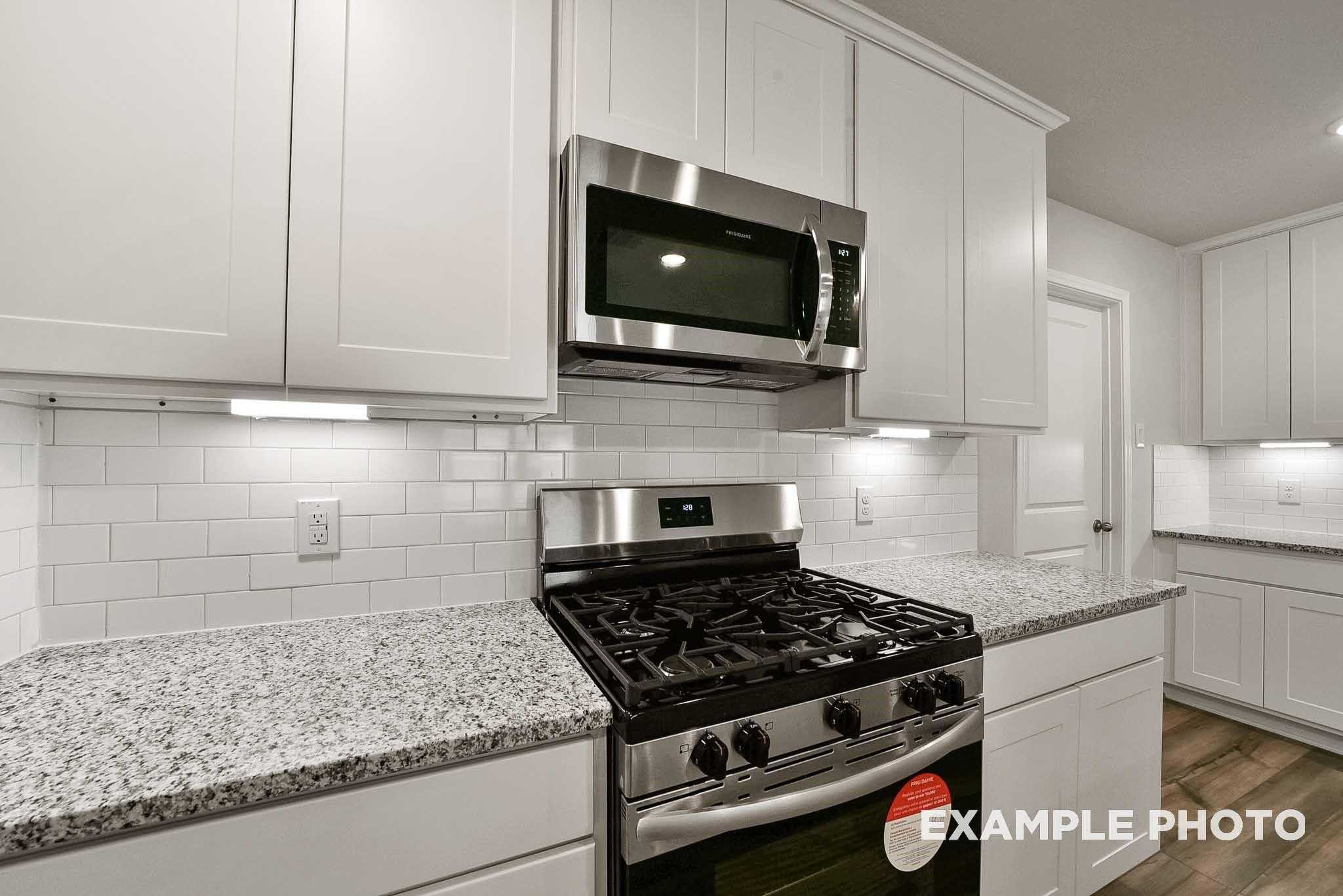 Bright kitchen with white cabinets, granite countertops, stainless steel gas range and microwave in Davidson Homes Tierra B, Beasley, Texas